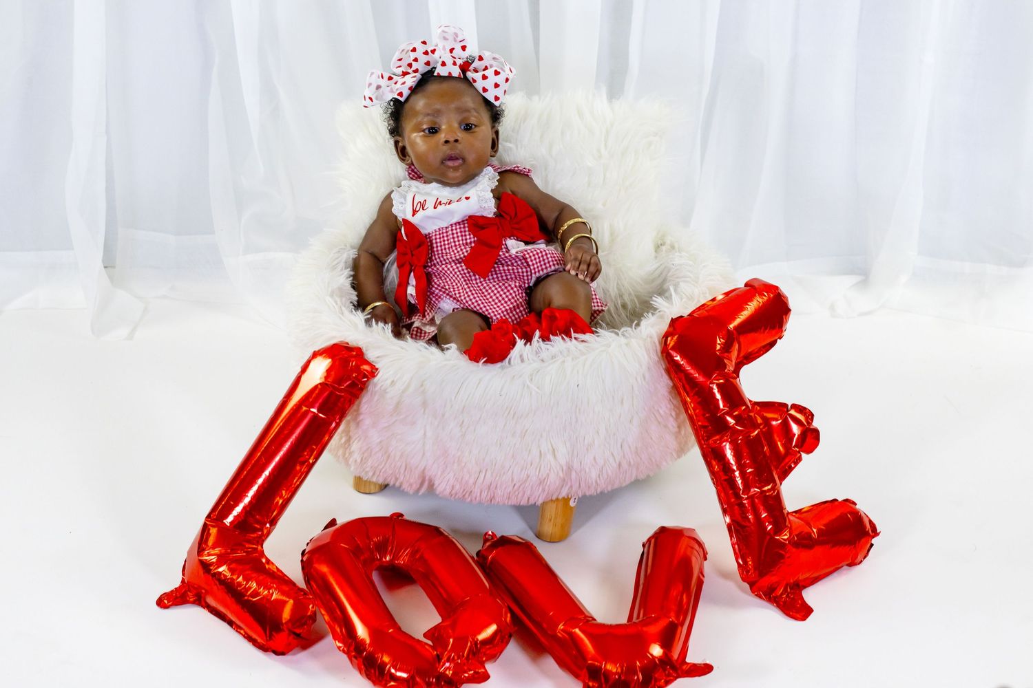 Black infant in Valentine's Day outfit sitting in fluffy basket with LOVE balloons.