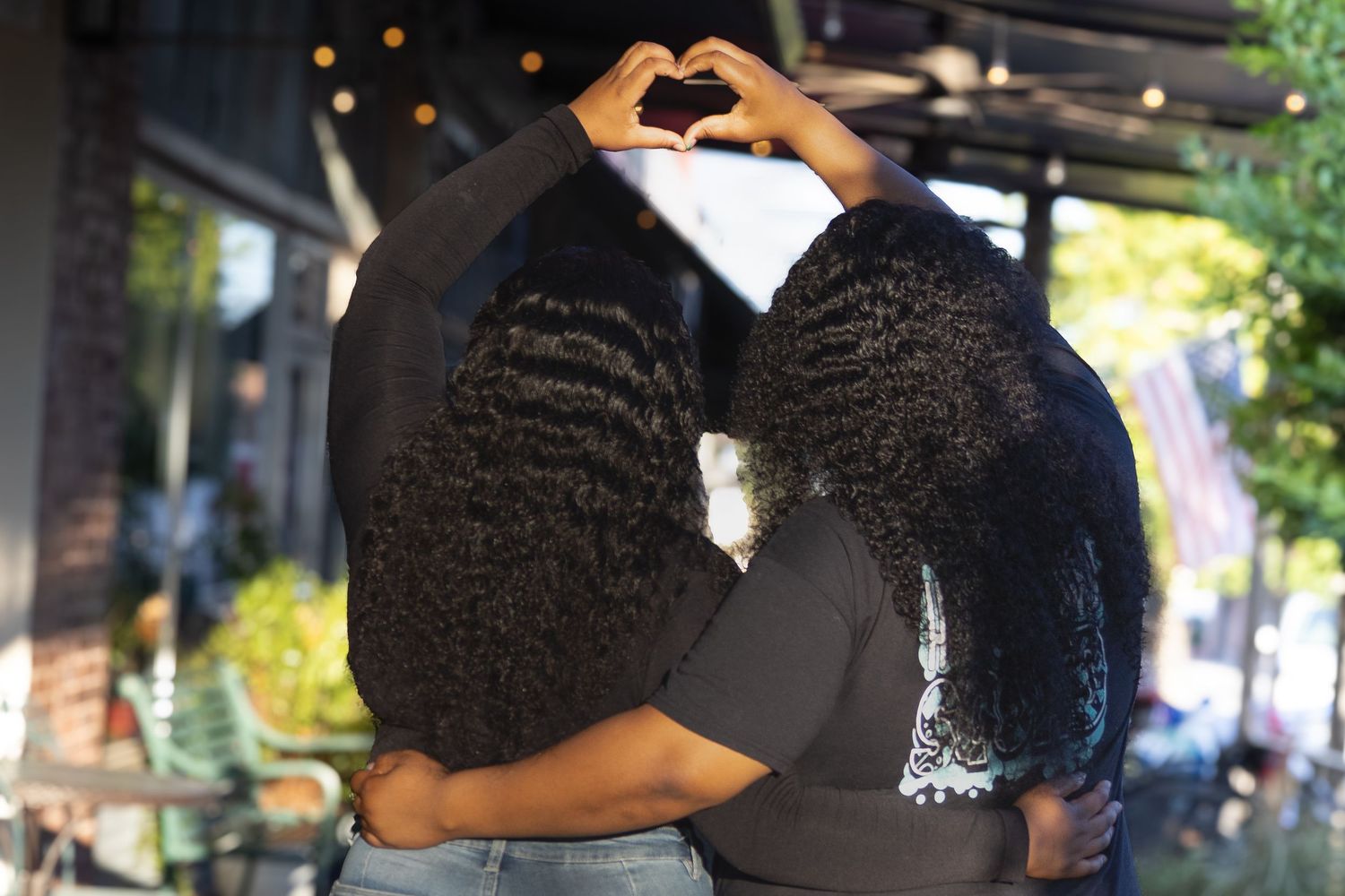 Two young Black women hugging and forming a heart shape with their hands above their heads.