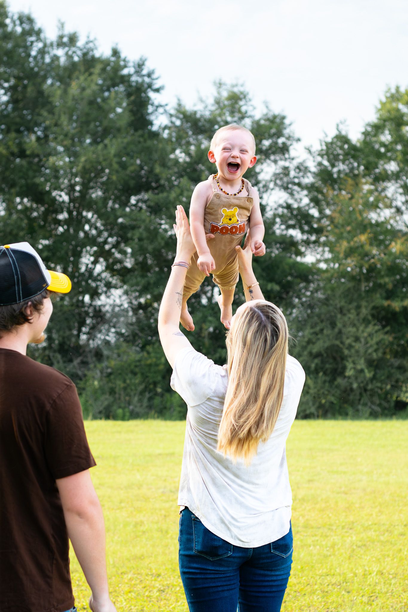Parents joyfully tossing their laughing baby in the air outdoors on a sunny day in a green park.