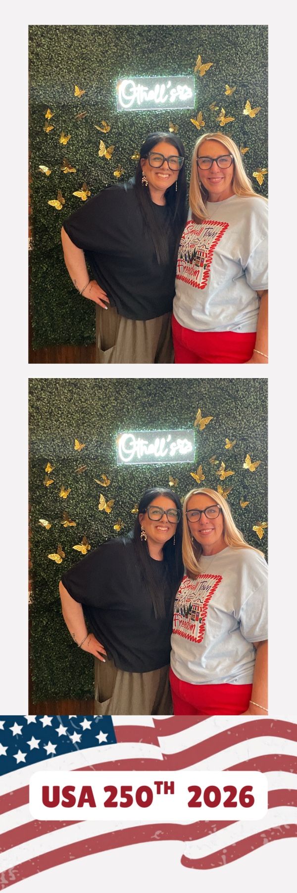 Two women wearing glasses pose together in front of a green hedge wall with gold butterflies and neon sign.