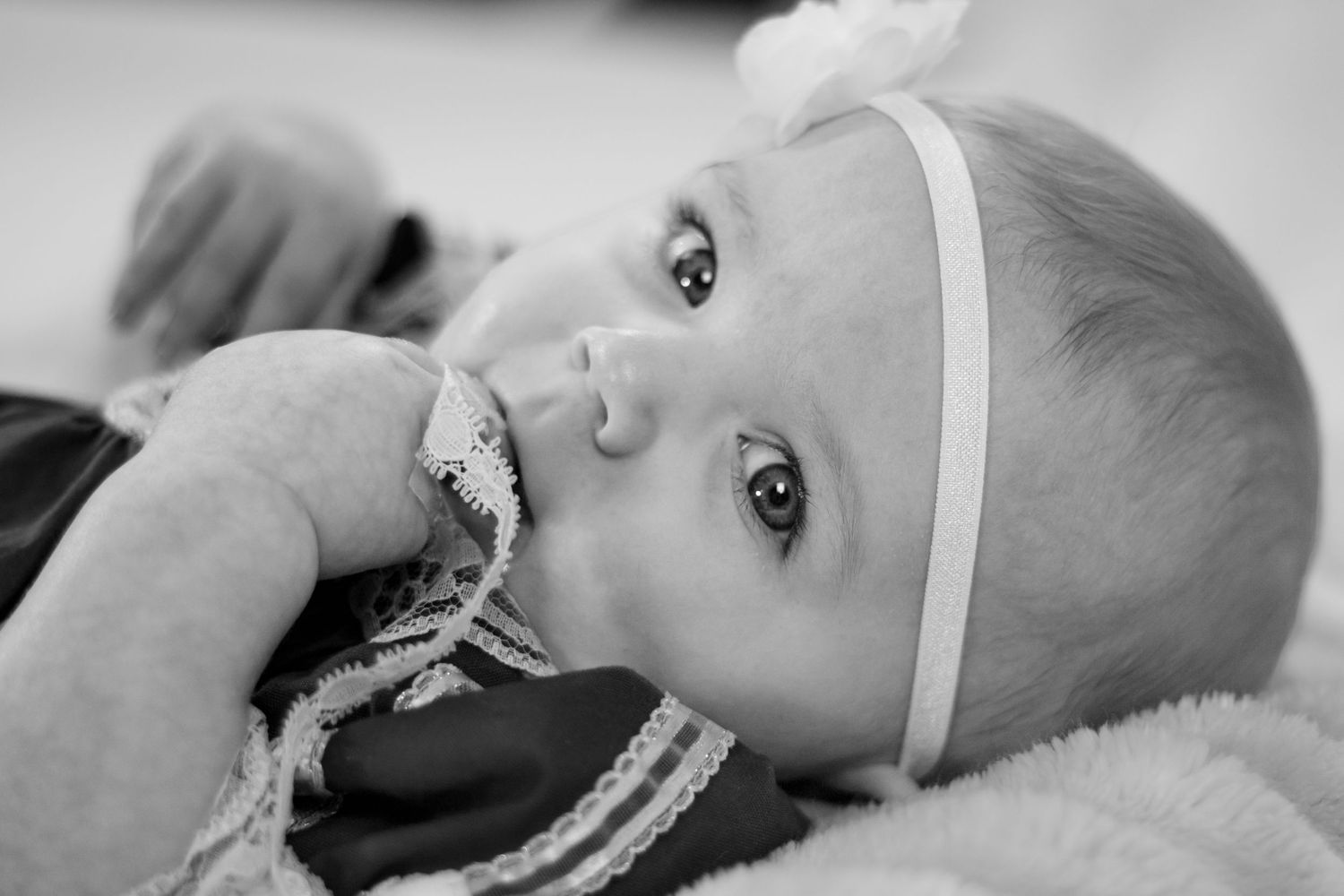 Black and white close-up of a baby girl in a lace outfit with a white flower headband lying down.