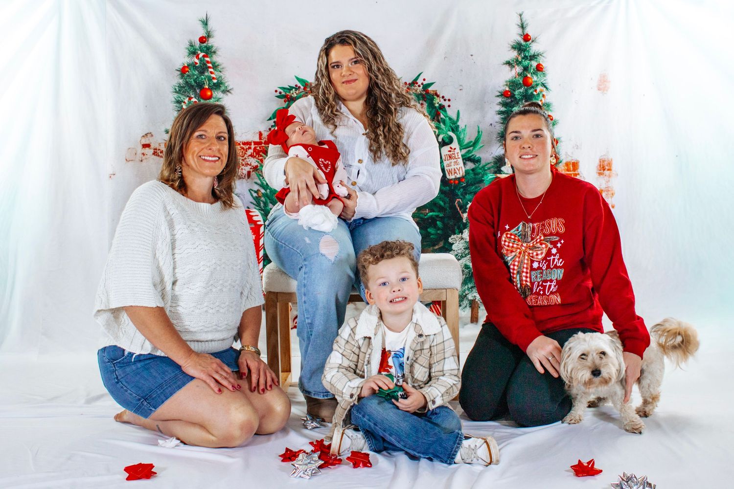 A family with a dog poses together in a bright Christmas studio with trees, wreaths, and holiday decorations.