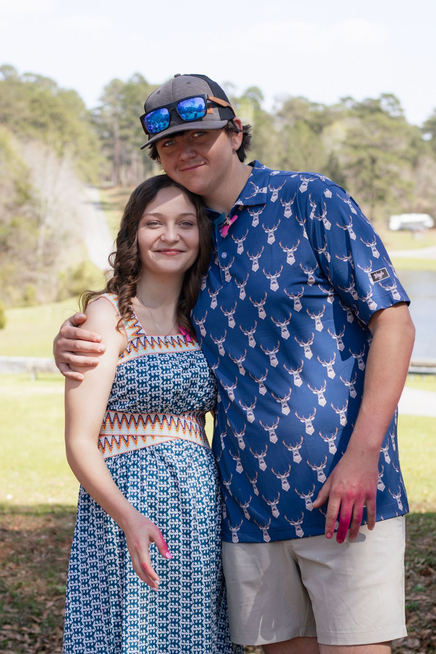 Teen couple poses together outdoors with pink gender reveal powder on hands.