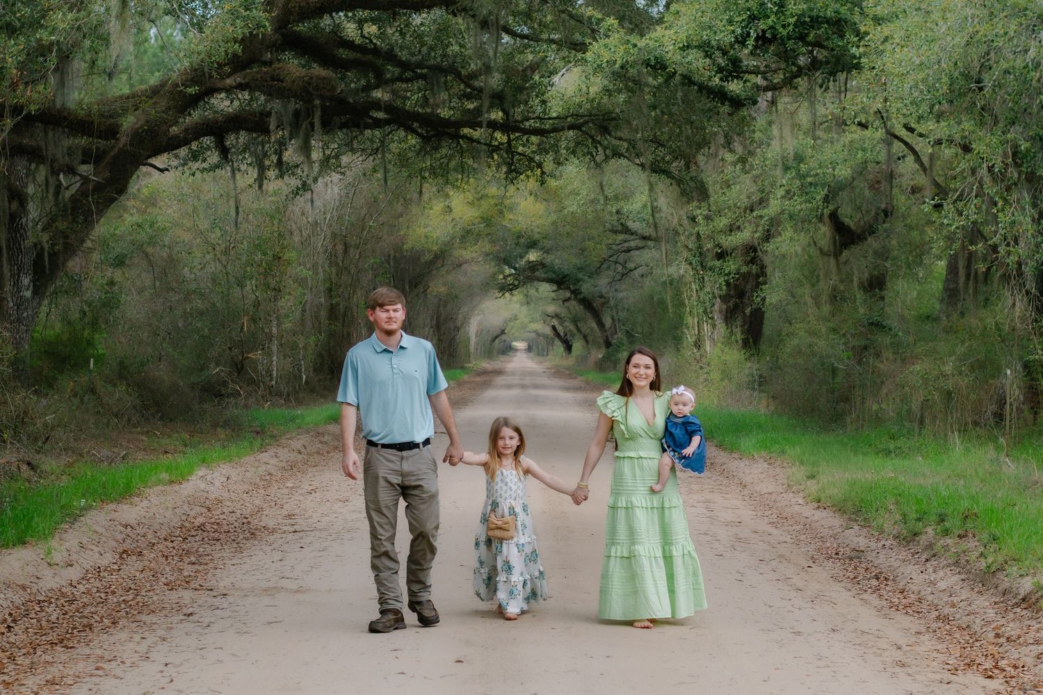 Happy family walking together on a beautiful canopied dirt road with sprawling oak trees overhead.