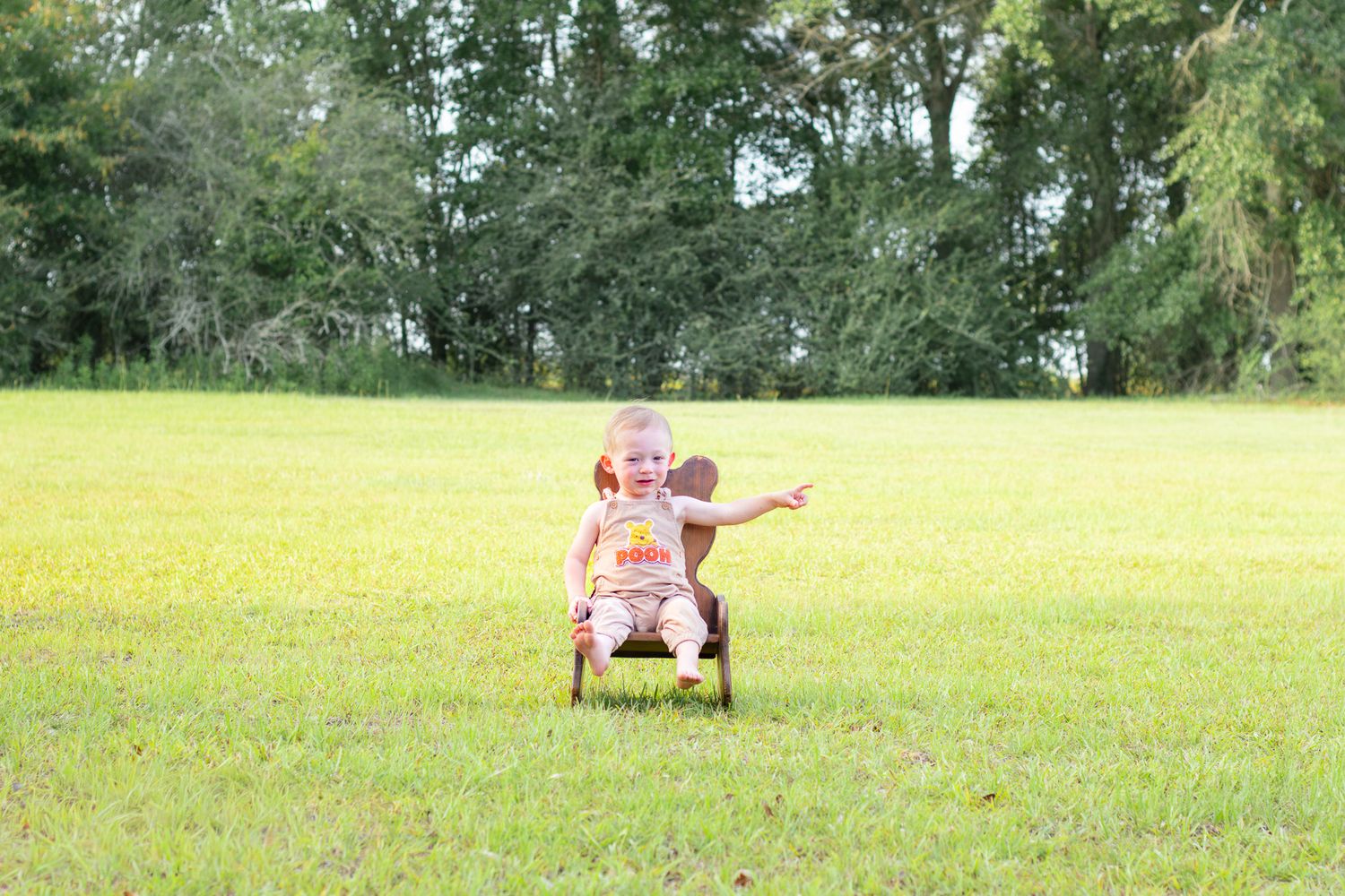 Young child sitting on a small ride-on toy in a lush green grassy field with trees in the background.