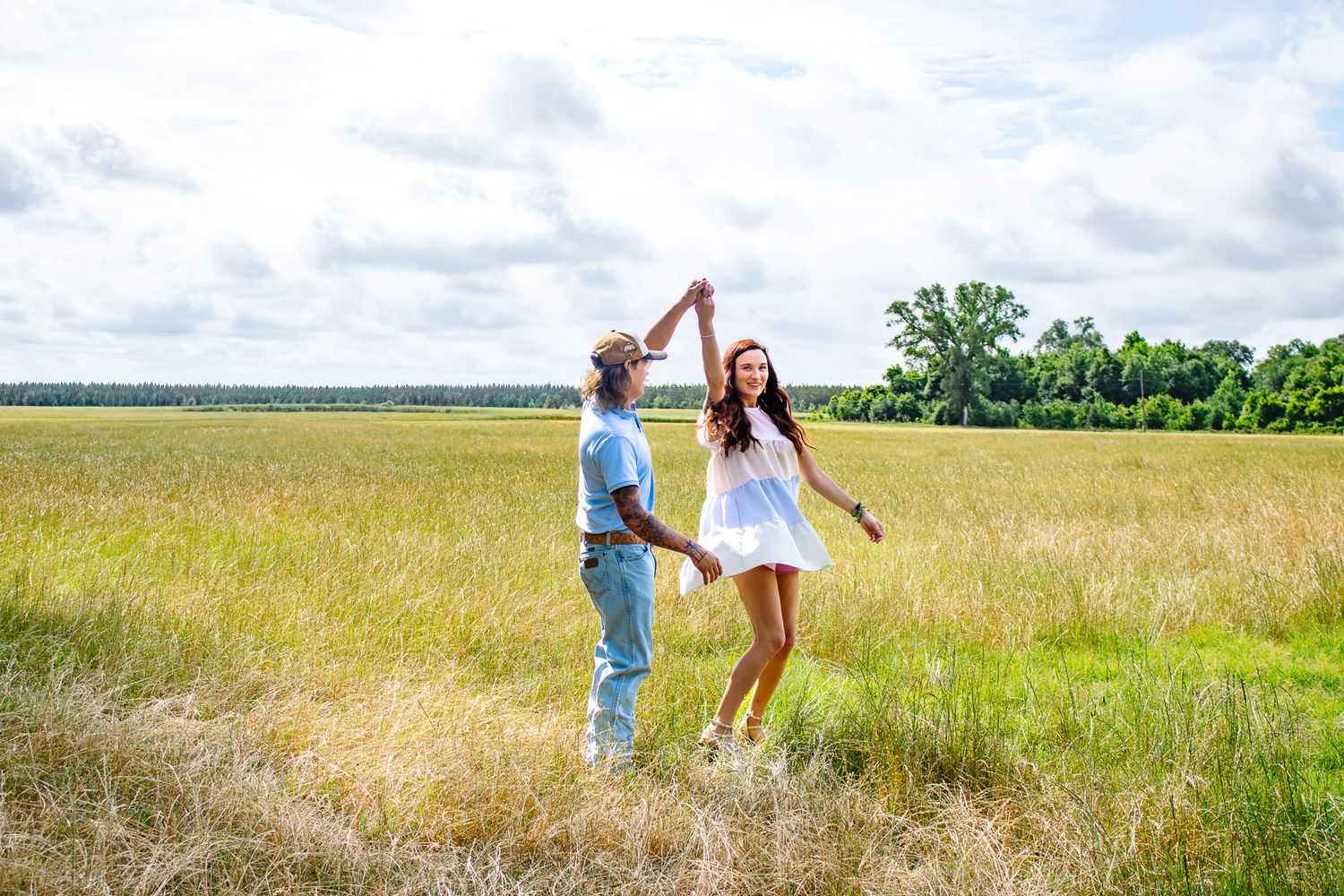 Couple dancing joyfully in a golden field, woman in white dress spinning under mans raised arm on cloudy day.