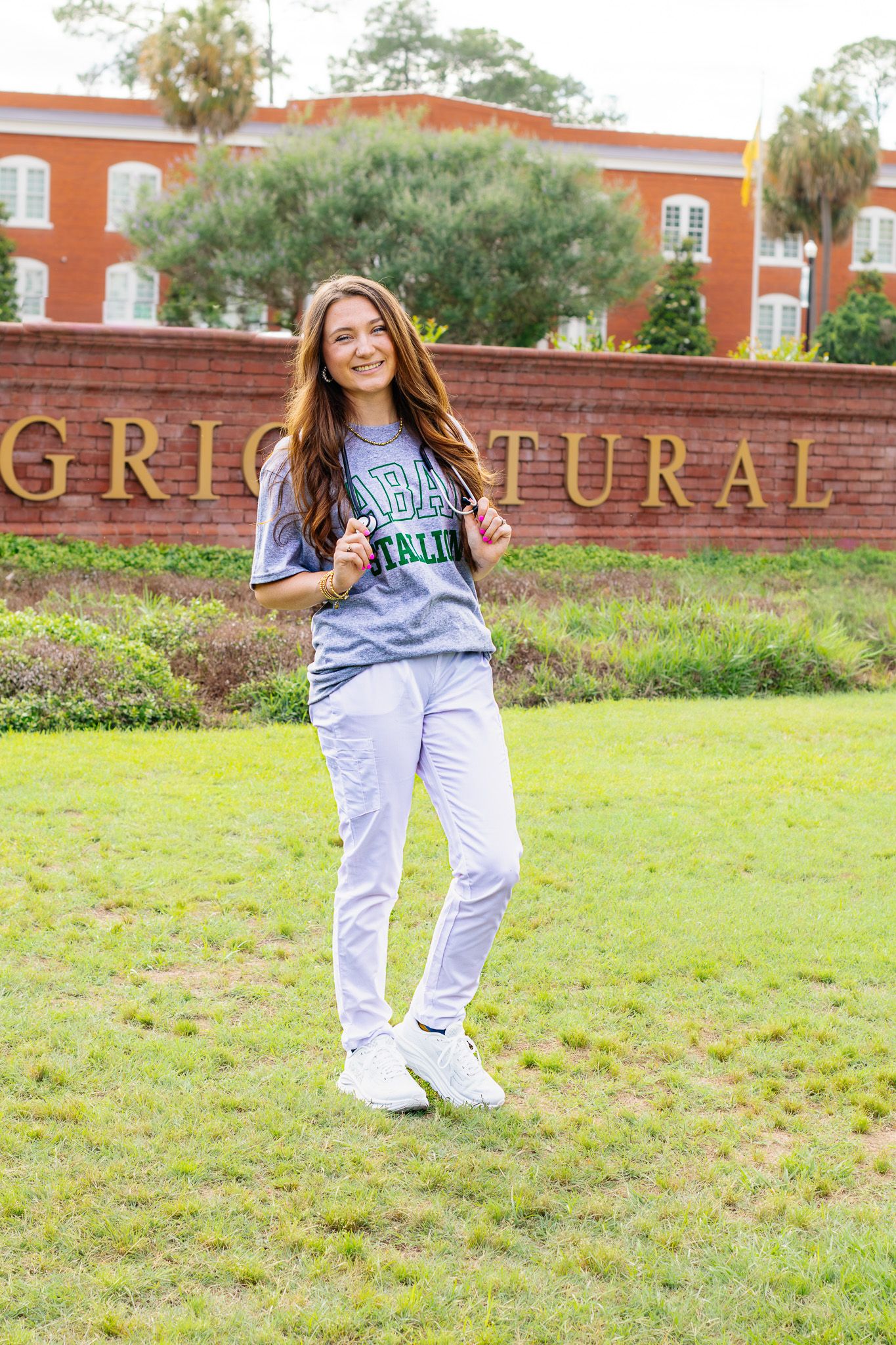 Smiling young woman in college athletic shirt posing in front of university agricultural brick sign.