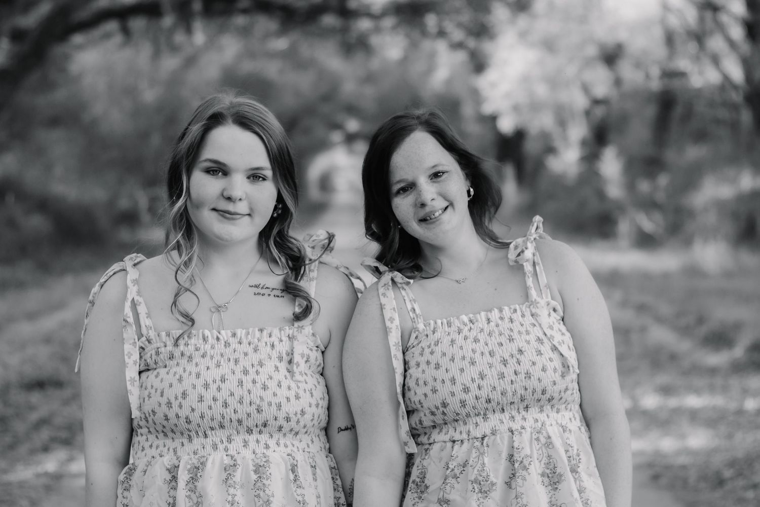 Two young women in matching floral sundresses pose together outdoors in a black and white photo.