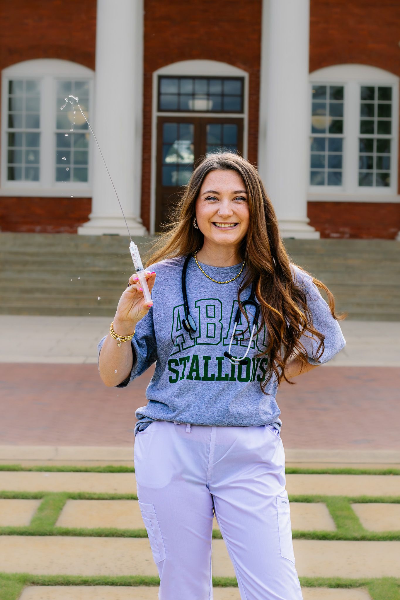 Smiling young woman in ABAC Stallions sweatshirt holding a sparkler in front of brick building.