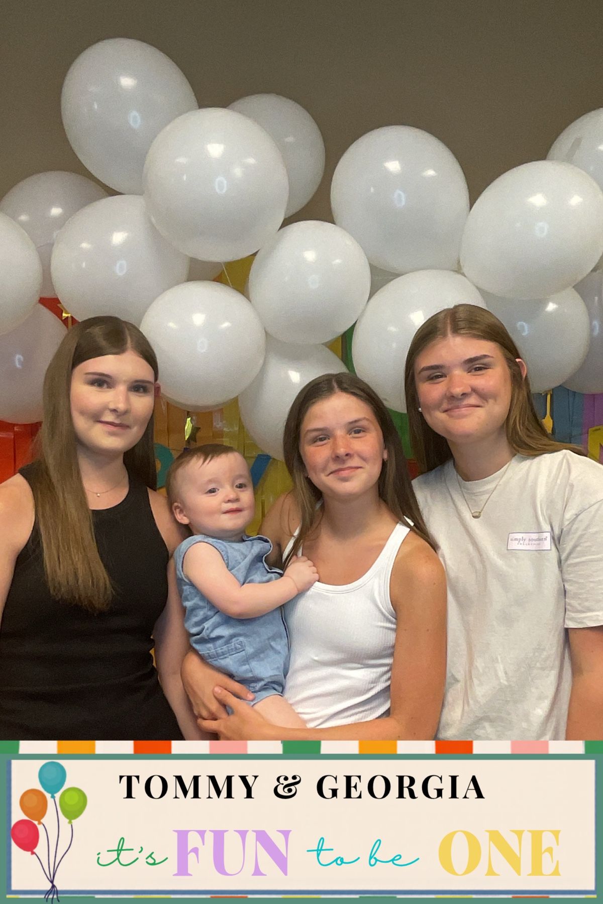 Four girls pose with a baby at Tommy and Georgia's first birthday party with white balloons.