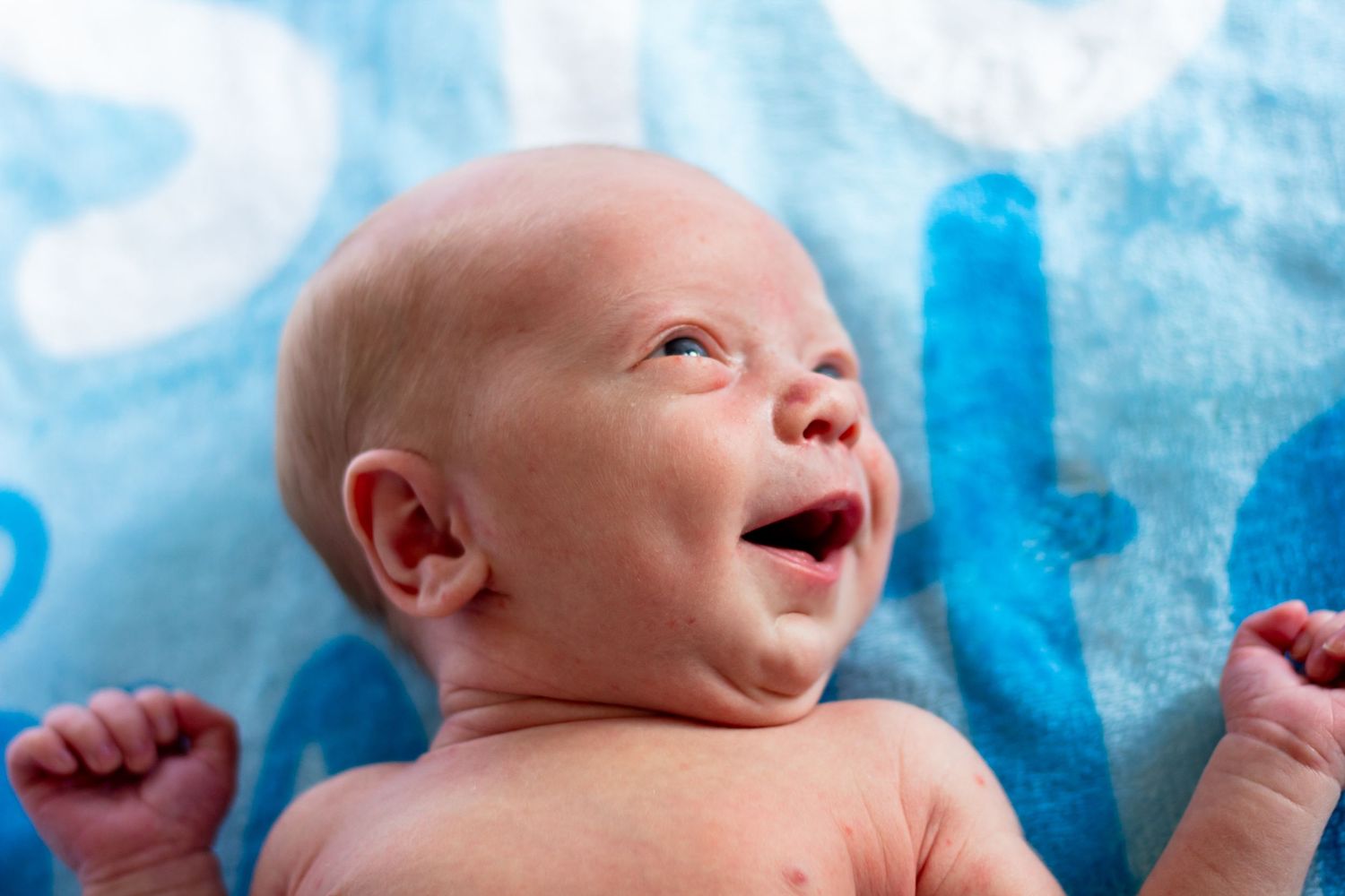 Newborn baby smiling and stretching arms while lying on a blue blanket.
