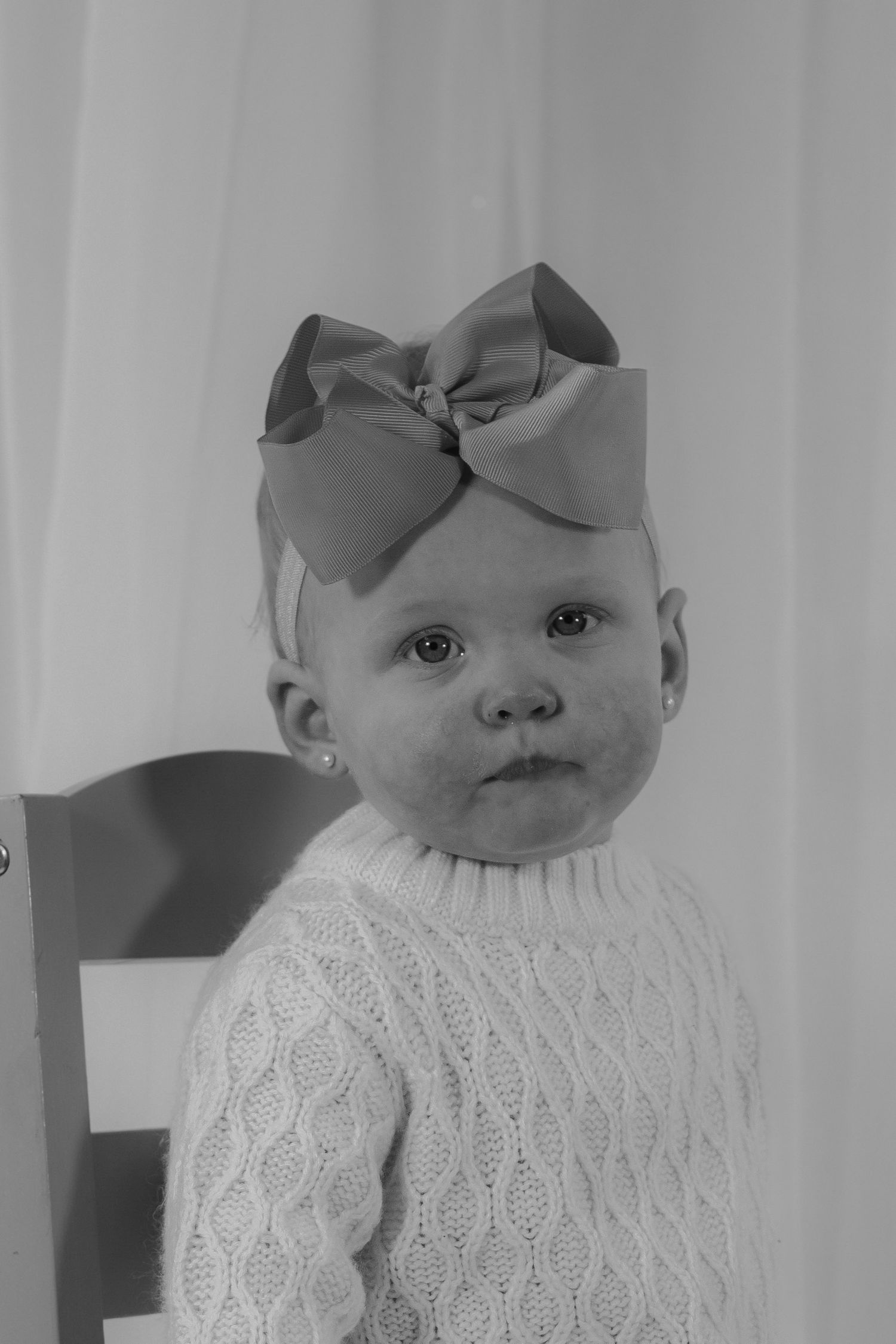 Black and white portrait of a baby girl in cable knit sweater wearing a large bow headband.