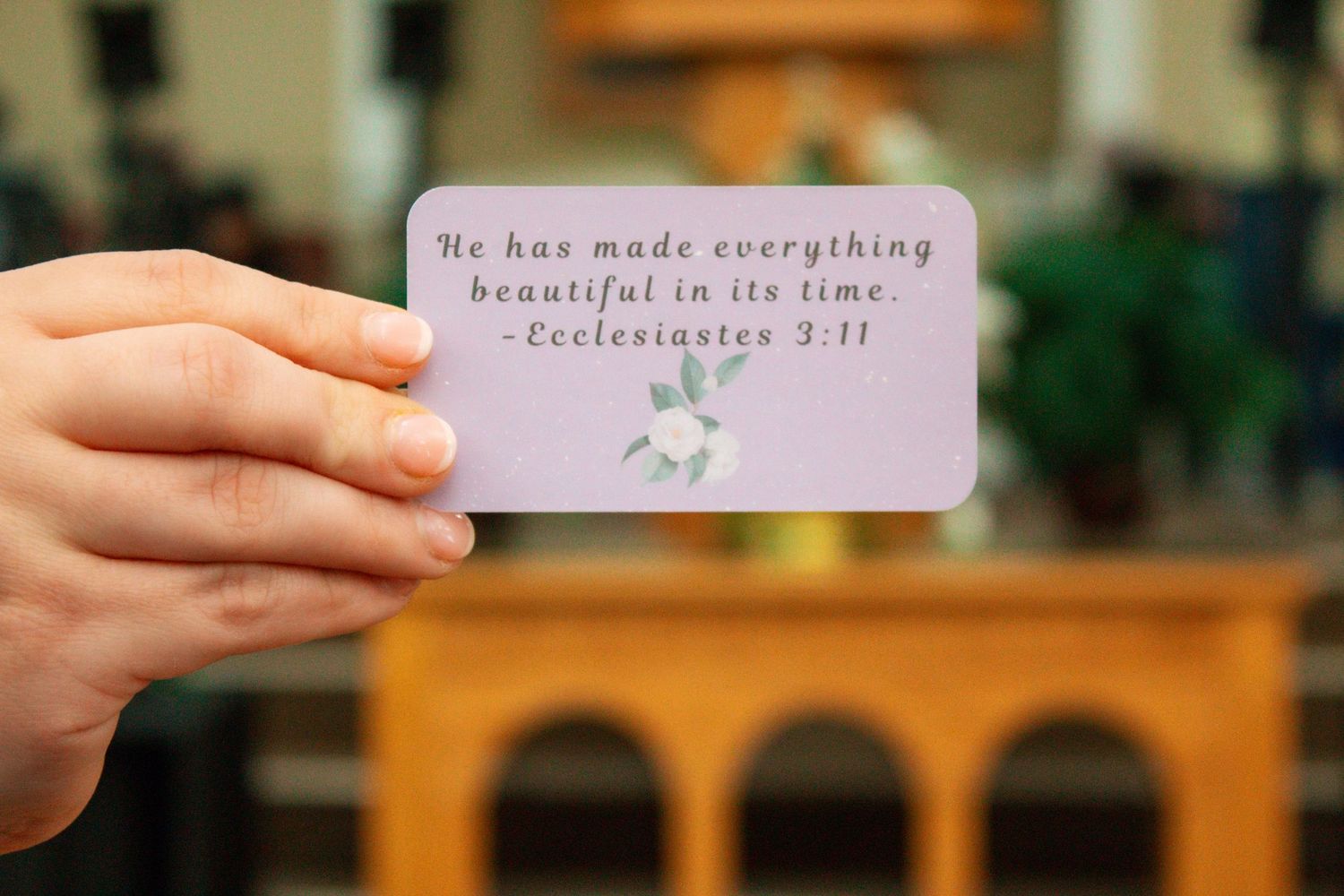 Hand holding a small card with Ecclesiastes 3:11 Bible verse quote in a church setting.