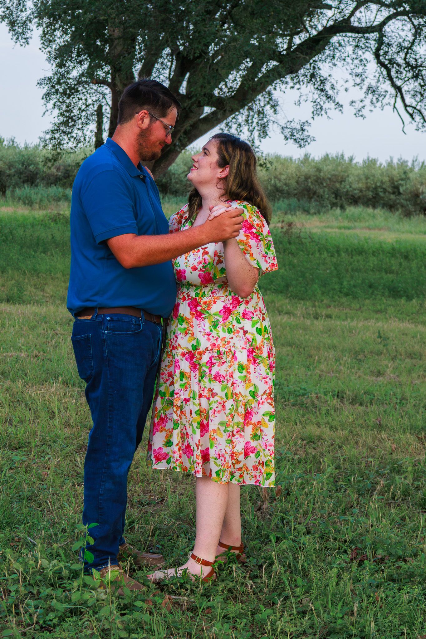 Couple sharing a romantic moment outdoors, man in blue shirt and woman in floral dress, standing in green field.