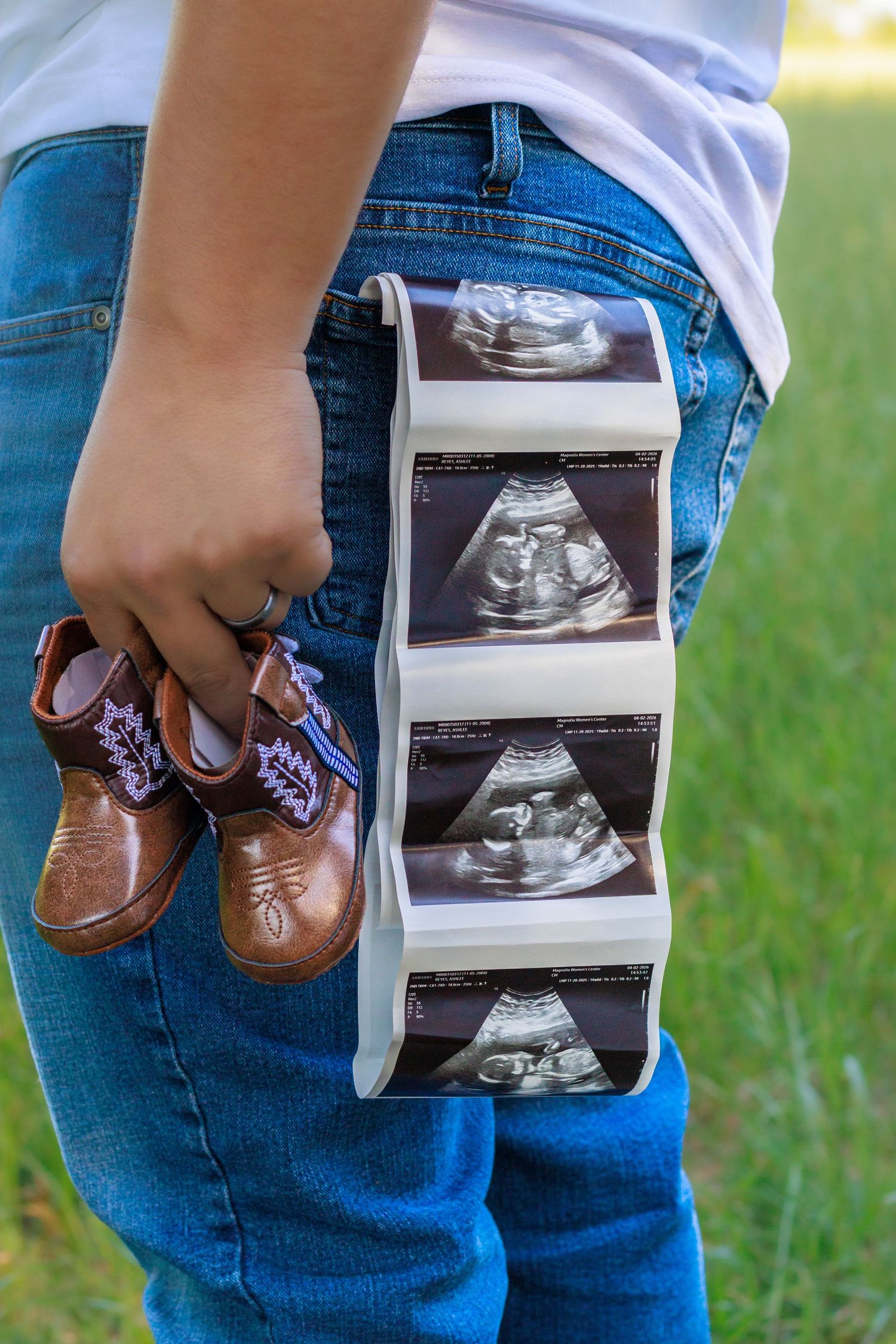 Person holding ultrasound photos and tiny cowboy boots behind their back in a pregnancy announcement photo.