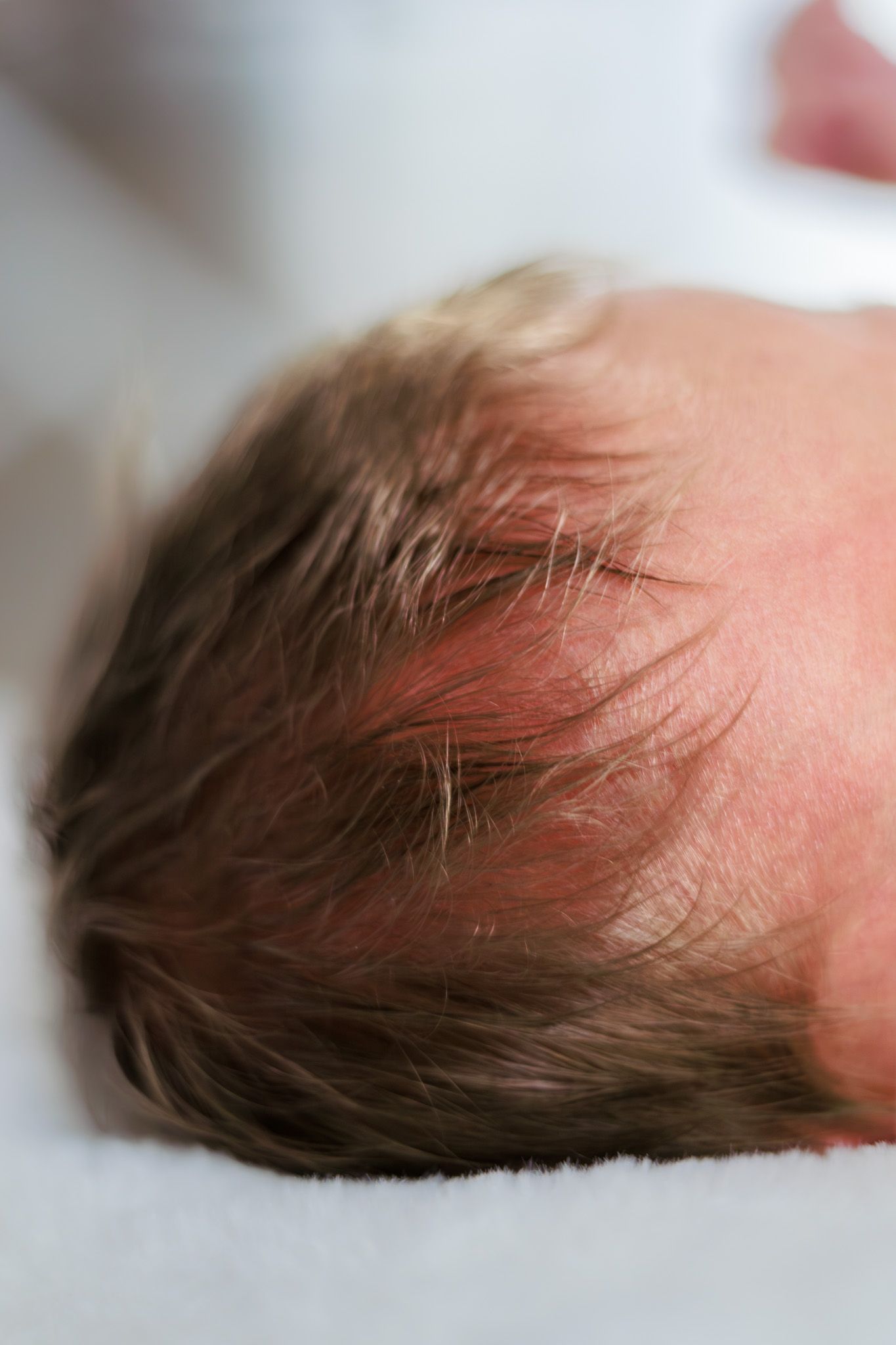Top view of a newborn baby's head with fine dark hair resting on white blanket.