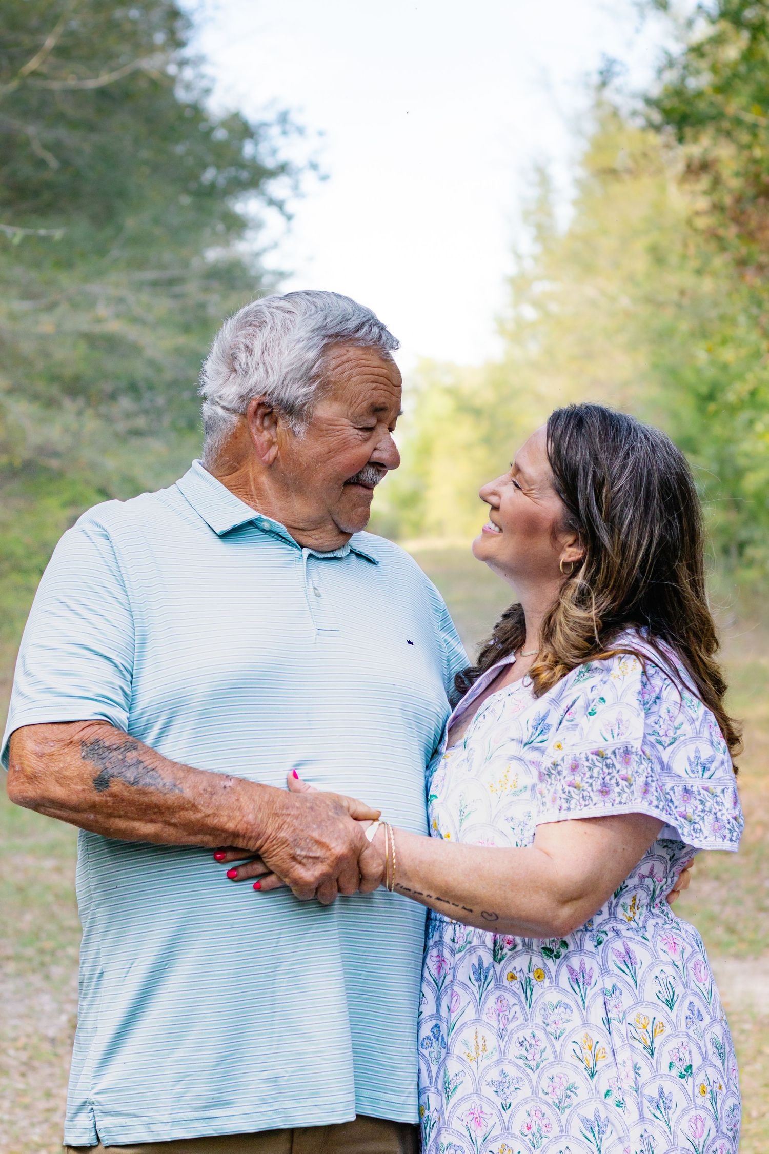 Joyful older couple laughing and holding hands together on a sunlit nature path.
