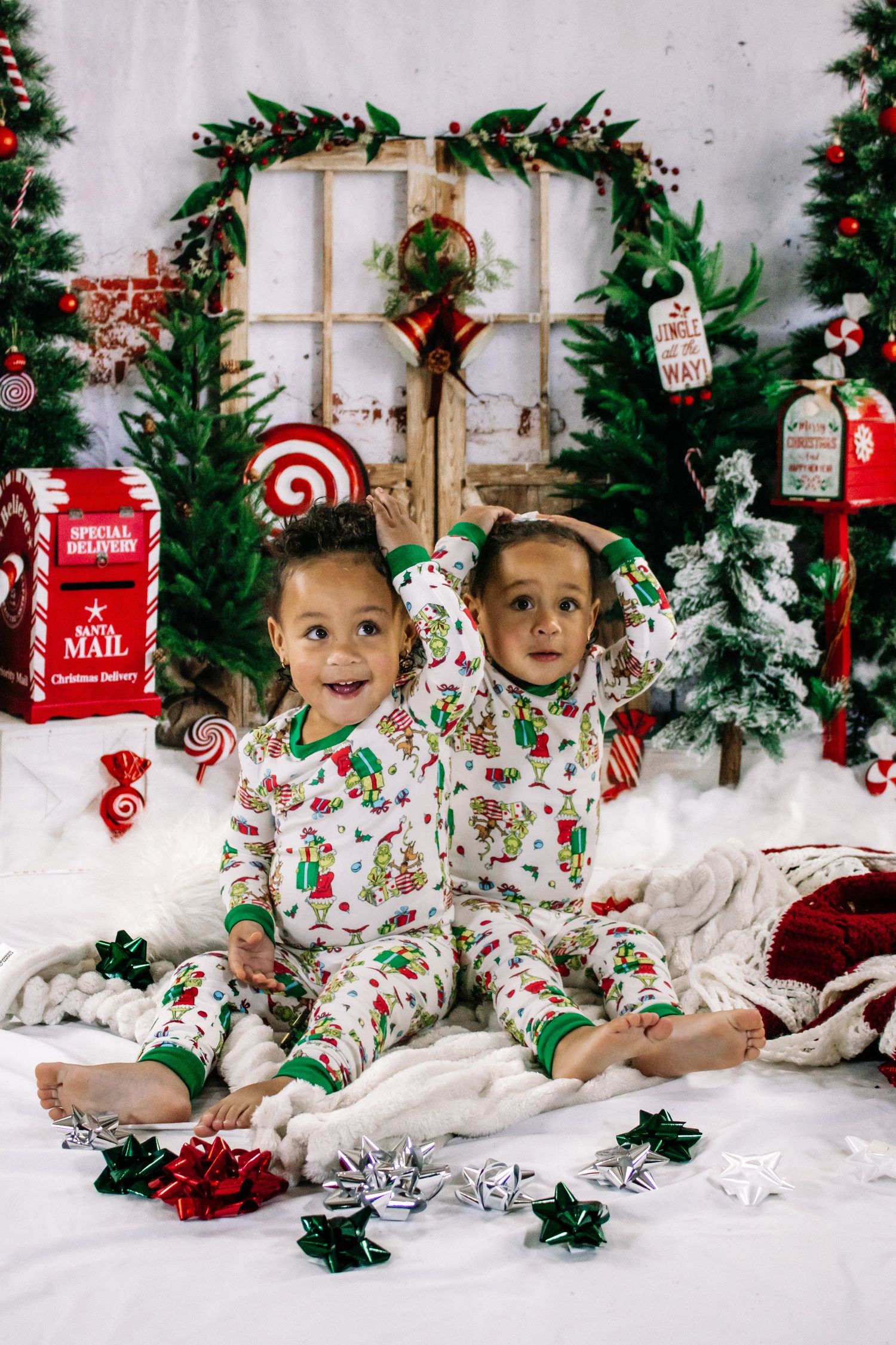 Two young children in matching Christmas pajamas posing with holiday decorations and gift bows.