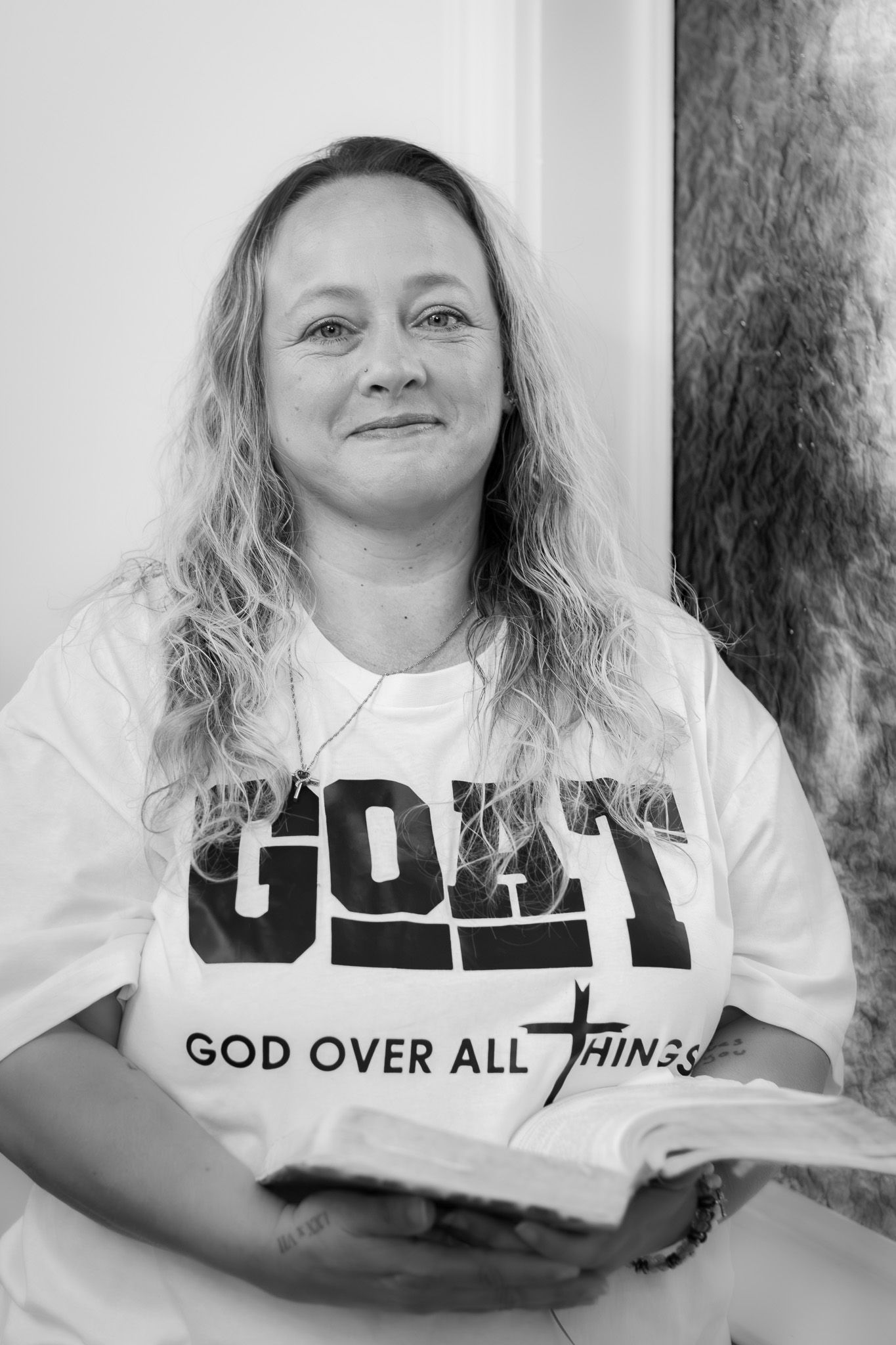 Black and white portrait of woman holding Bible wearing God Over All Things shirt.