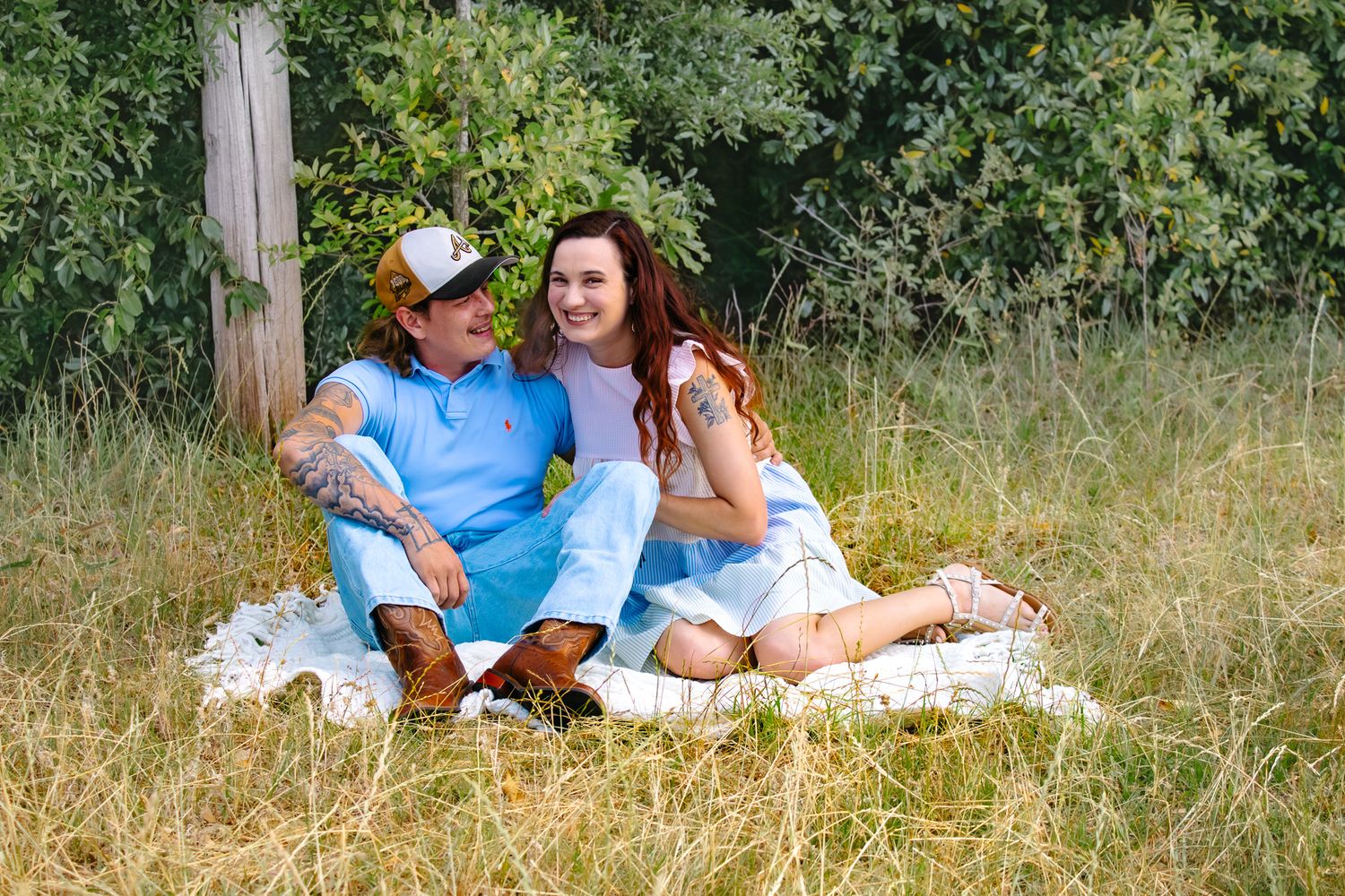 Happy couple relaxing on a blanket in a sunny meadow with green trees in background.