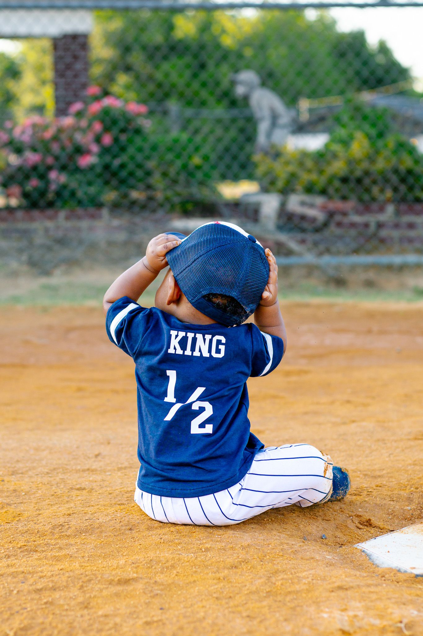 Baby in blue King 1/2 baseball jersey sitting on field base.
