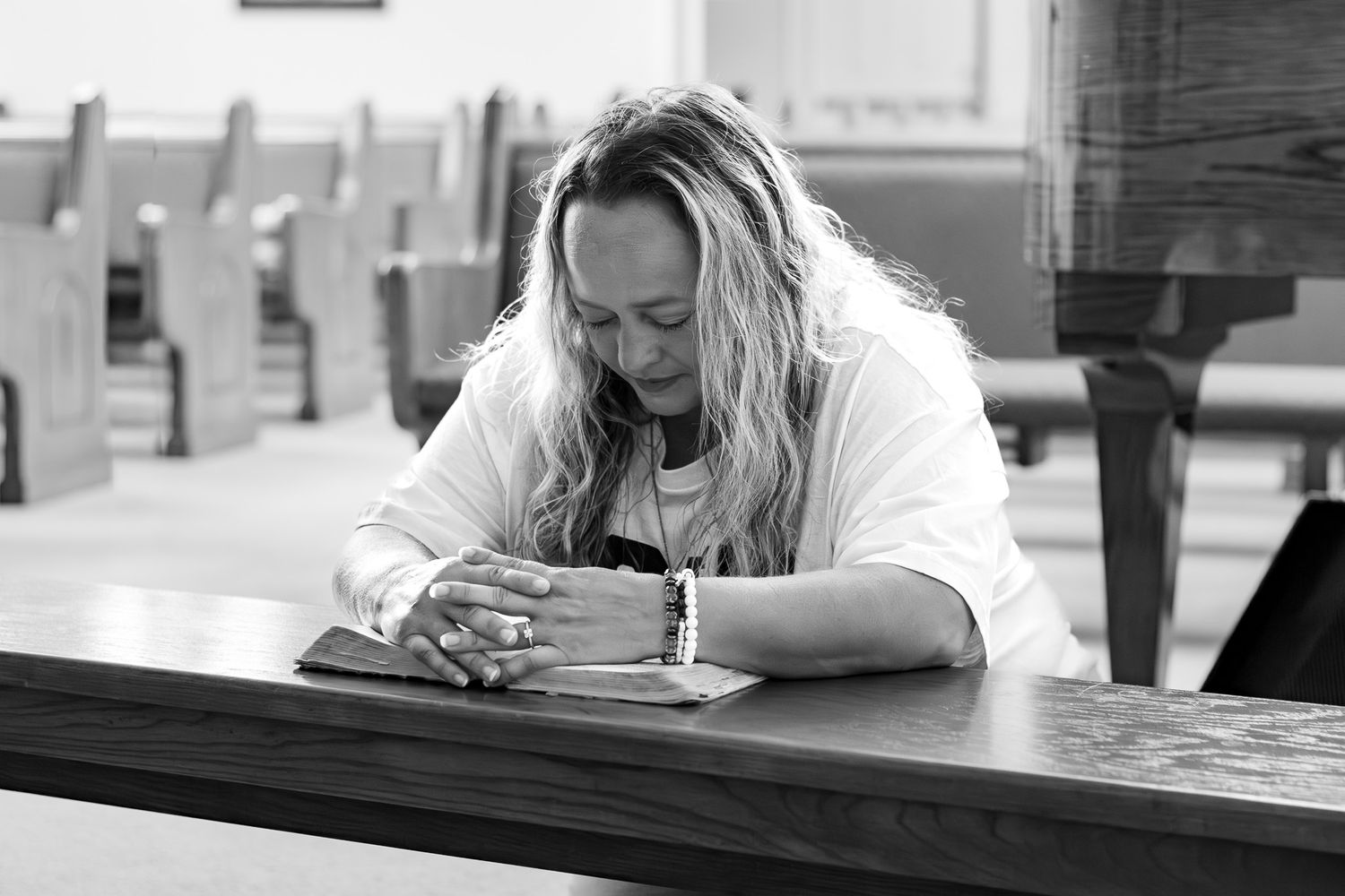 Woman praying over Bible in church pew, black and white photo of faithful worshipper in quiet devotion.