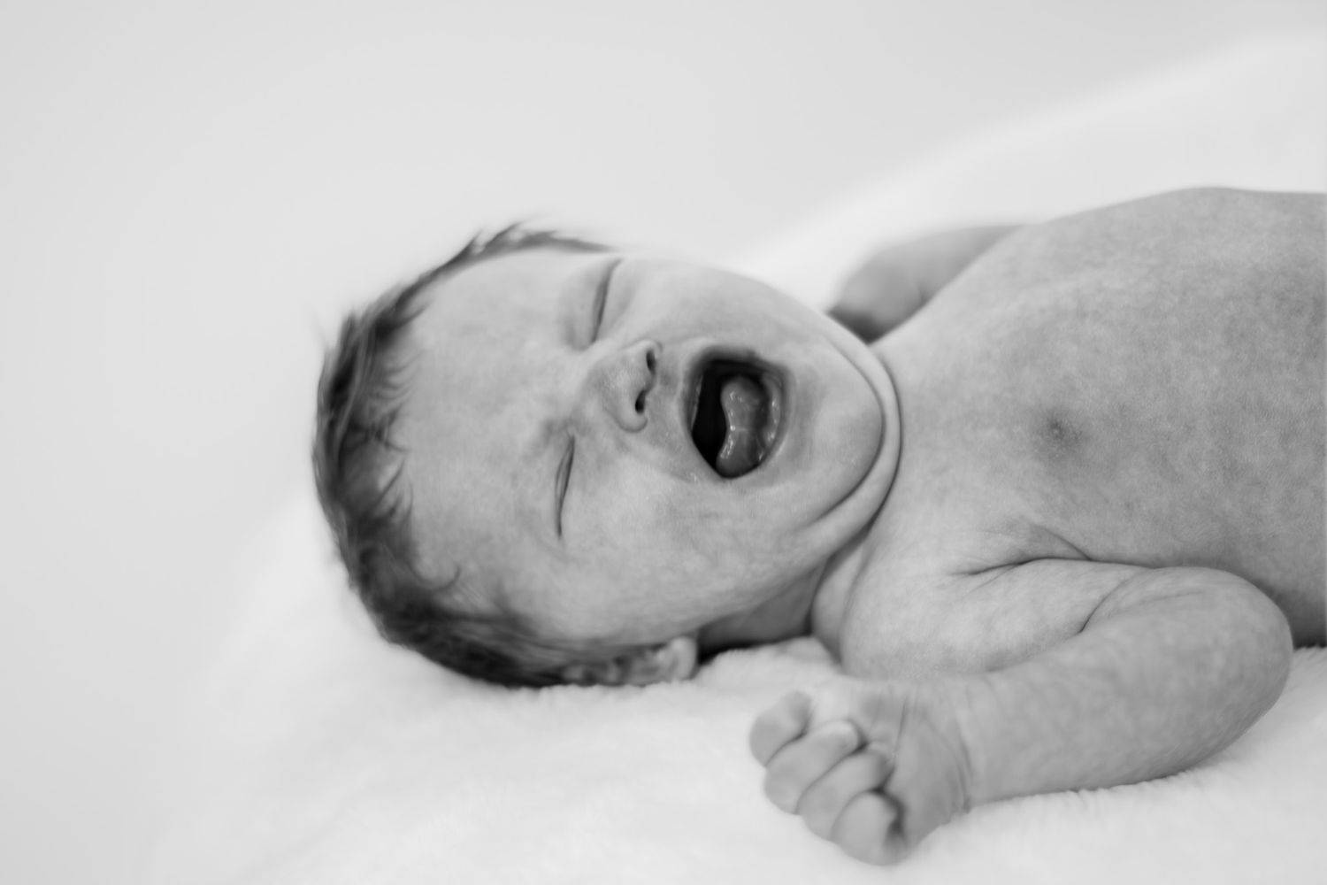 Black and white photo of a crying newborn baby lying on a white blanket.