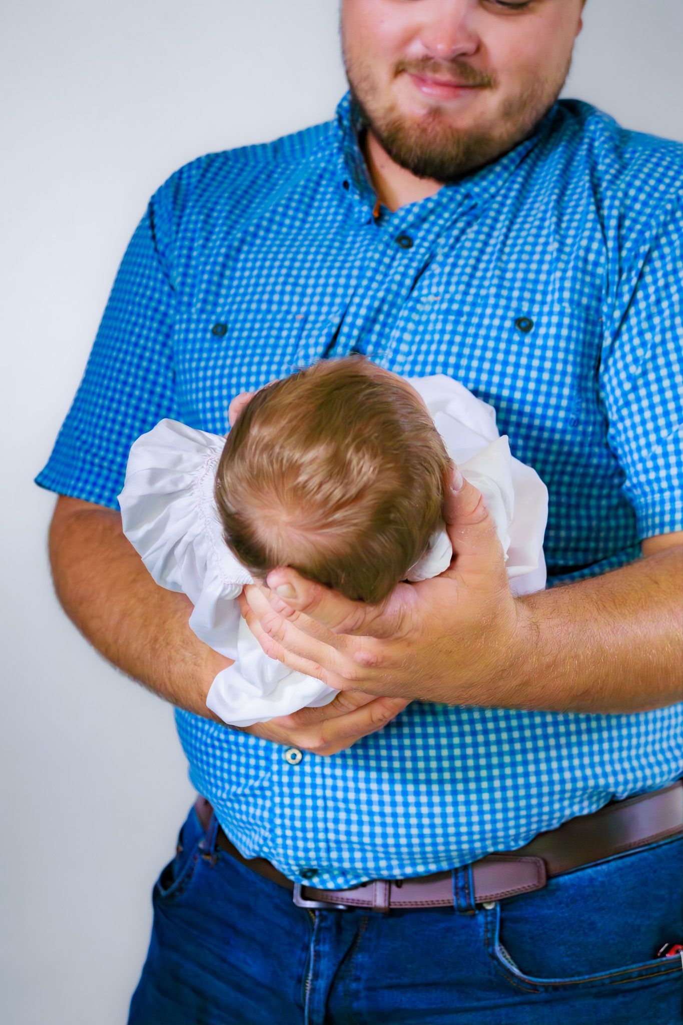 Bearded father in blue plaid shirt gently cradling his newborn baby.
