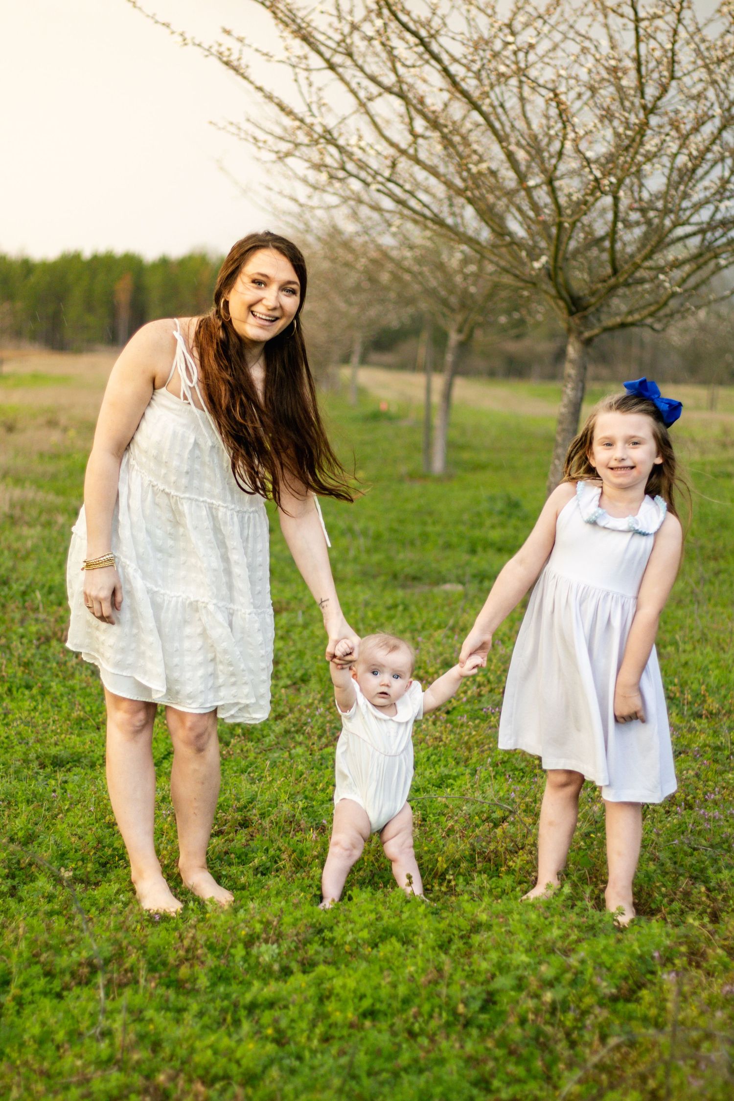 Happy mother and two children holding hands in a sunny green field outdoors.