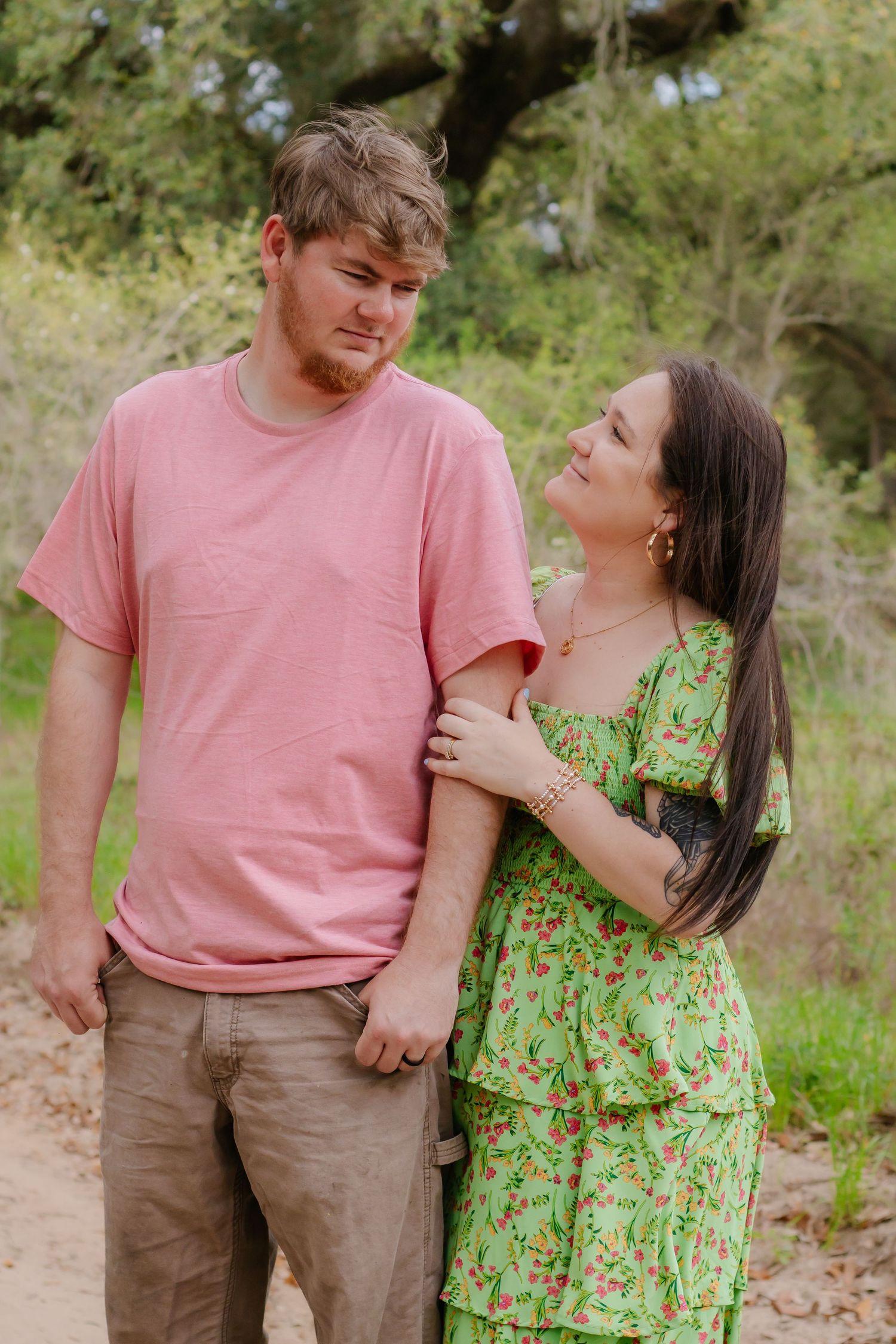 Young couple sharing a tender moment on a sandy path surrounded by green trees in spring.