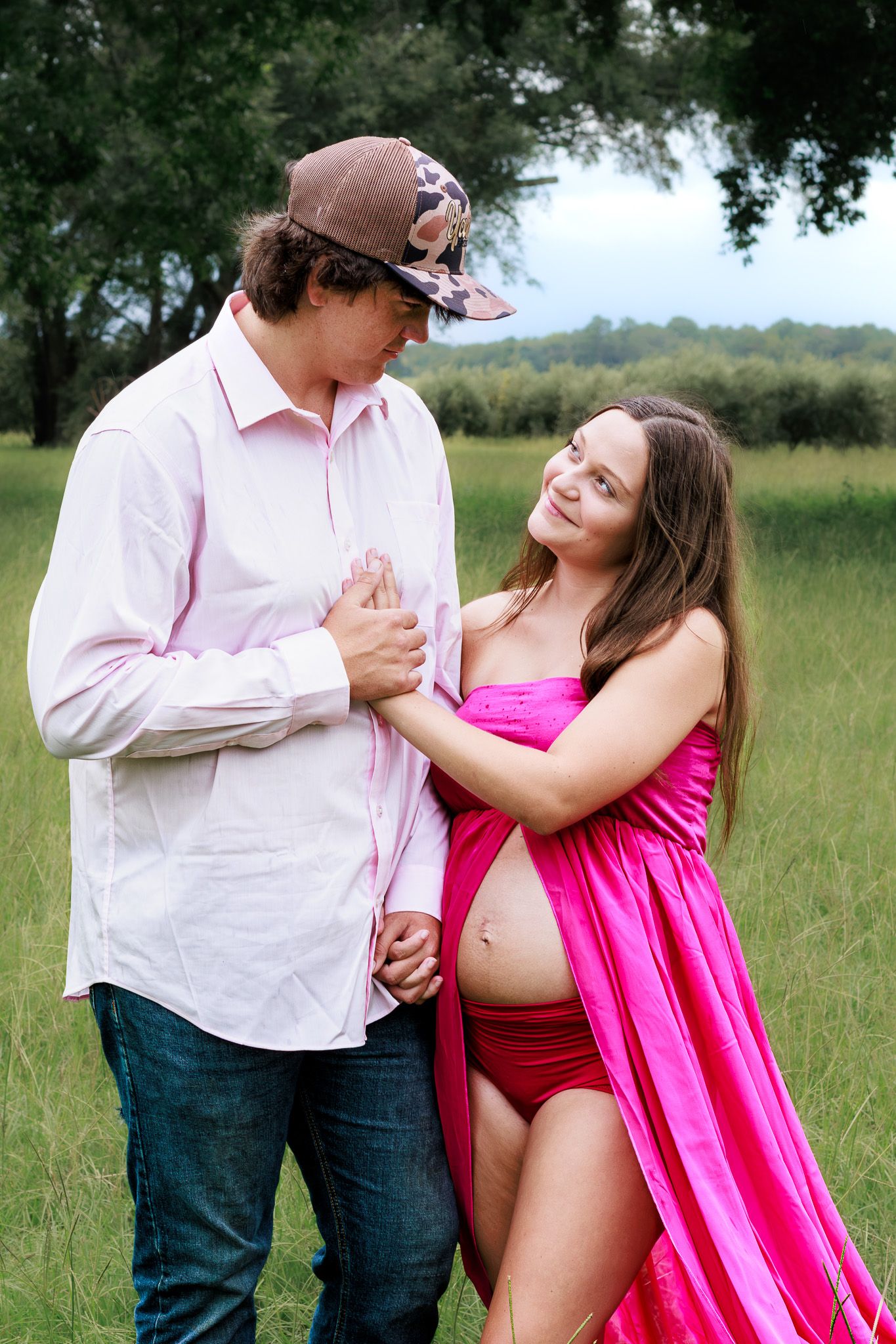 Happy couple sharing tender moment in field, pregnant woman in pink dress.