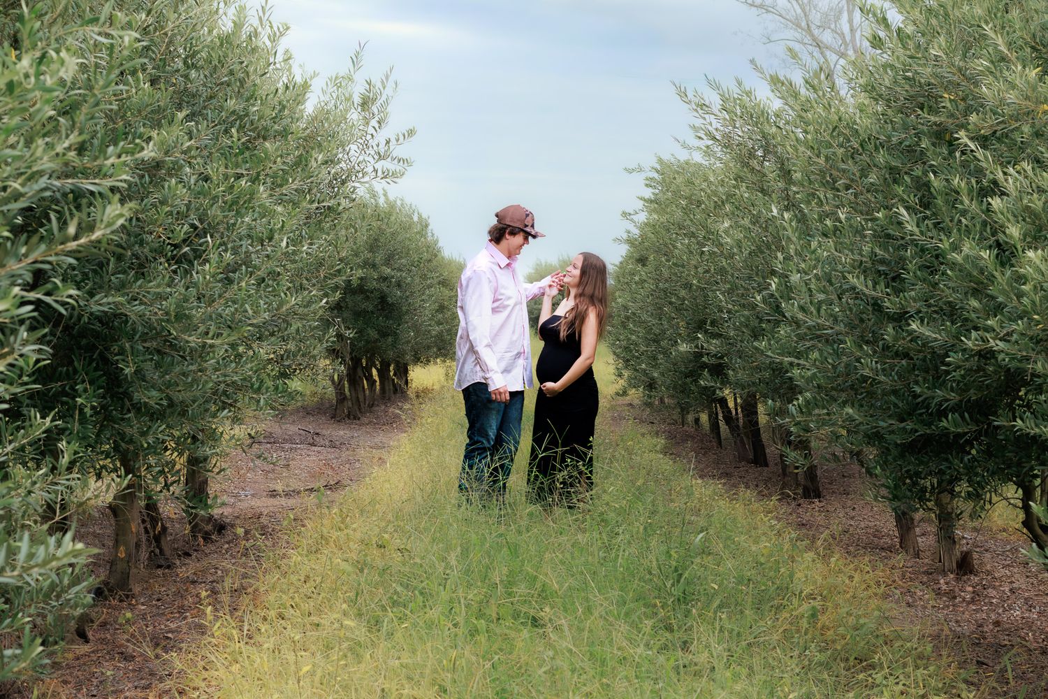Couple sharing a romantic moment in a lush green olive tree orchard pathway.