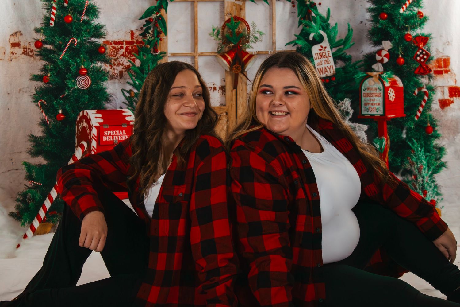 Two women in matching red plaid shirts sitting together in front of festive Christmas decor.