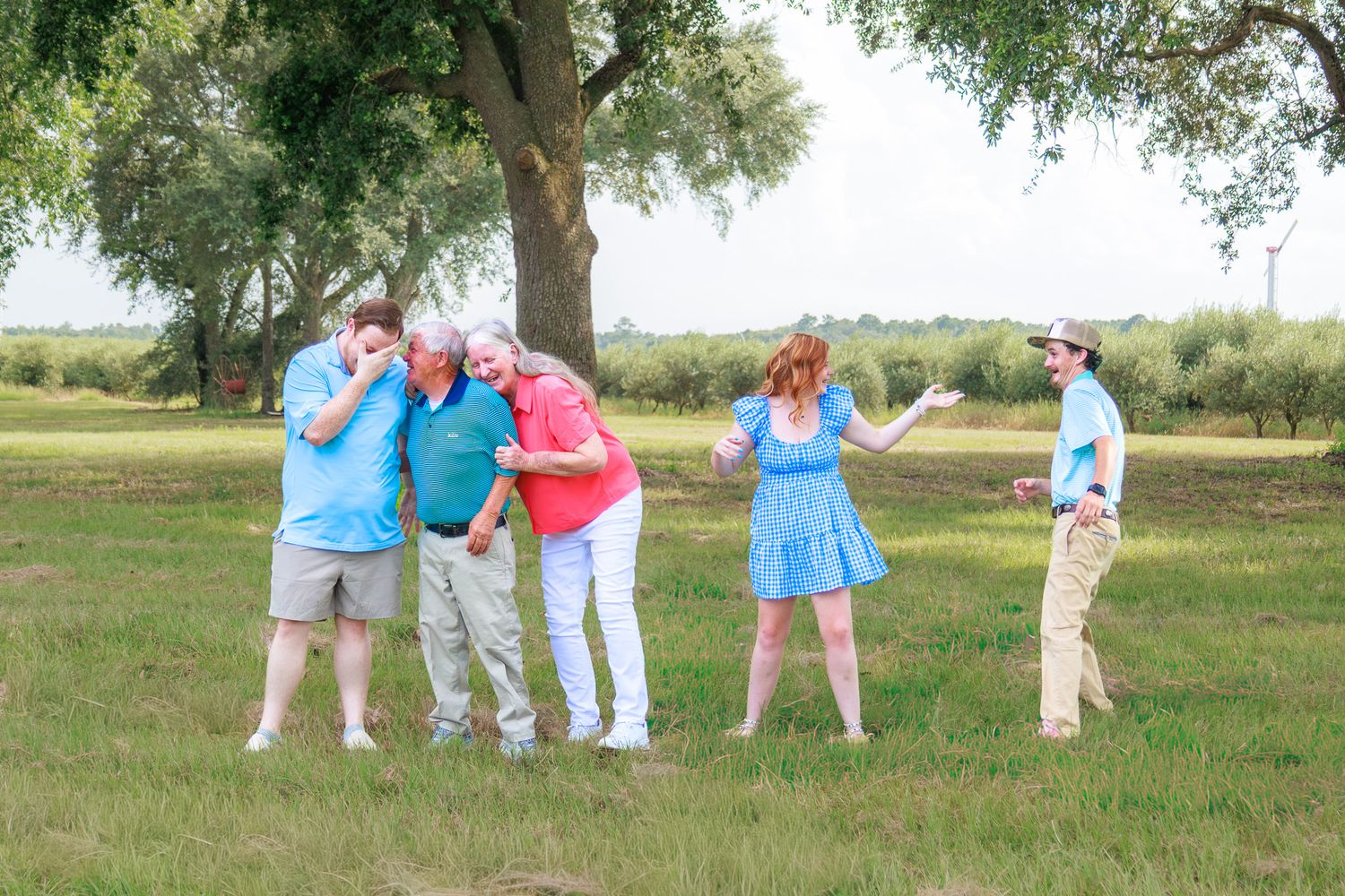 Group of five adults playing a fun outdoor game on green grass near large trees on a sunny day.