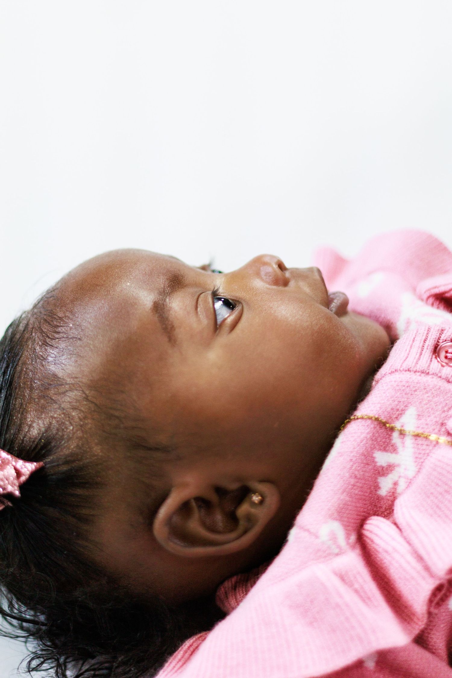 Sweet baby girl in pink outfit lying down with eyes partially closed in profile view.