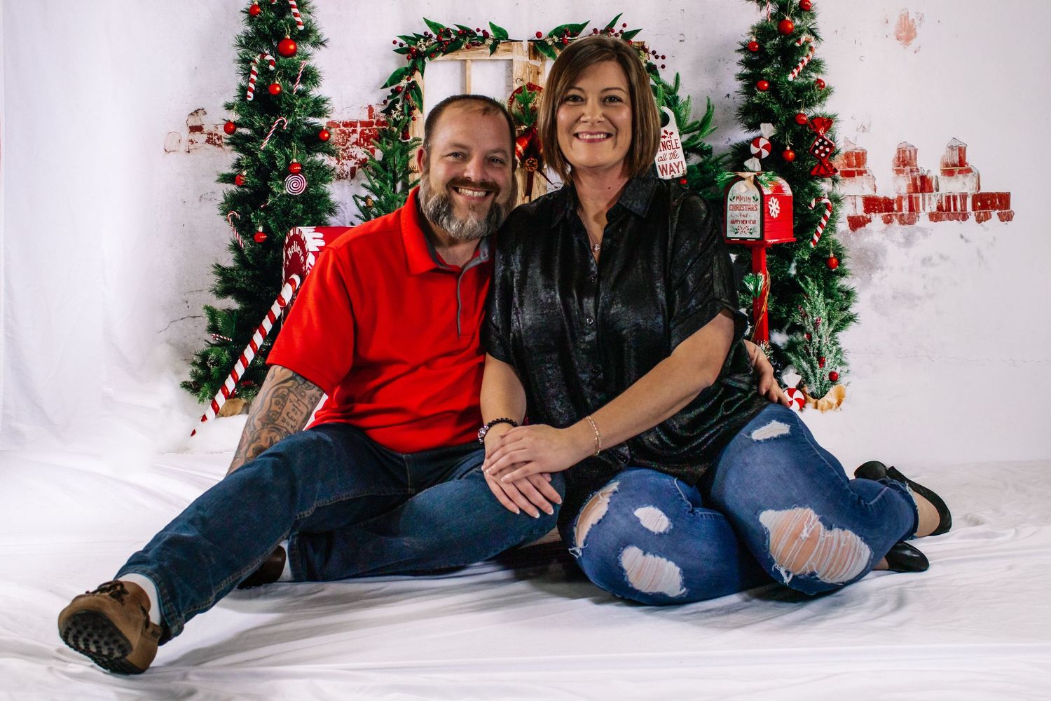 Couple sitting together smiling in front of Christmas holiday photo backdrop with garland.