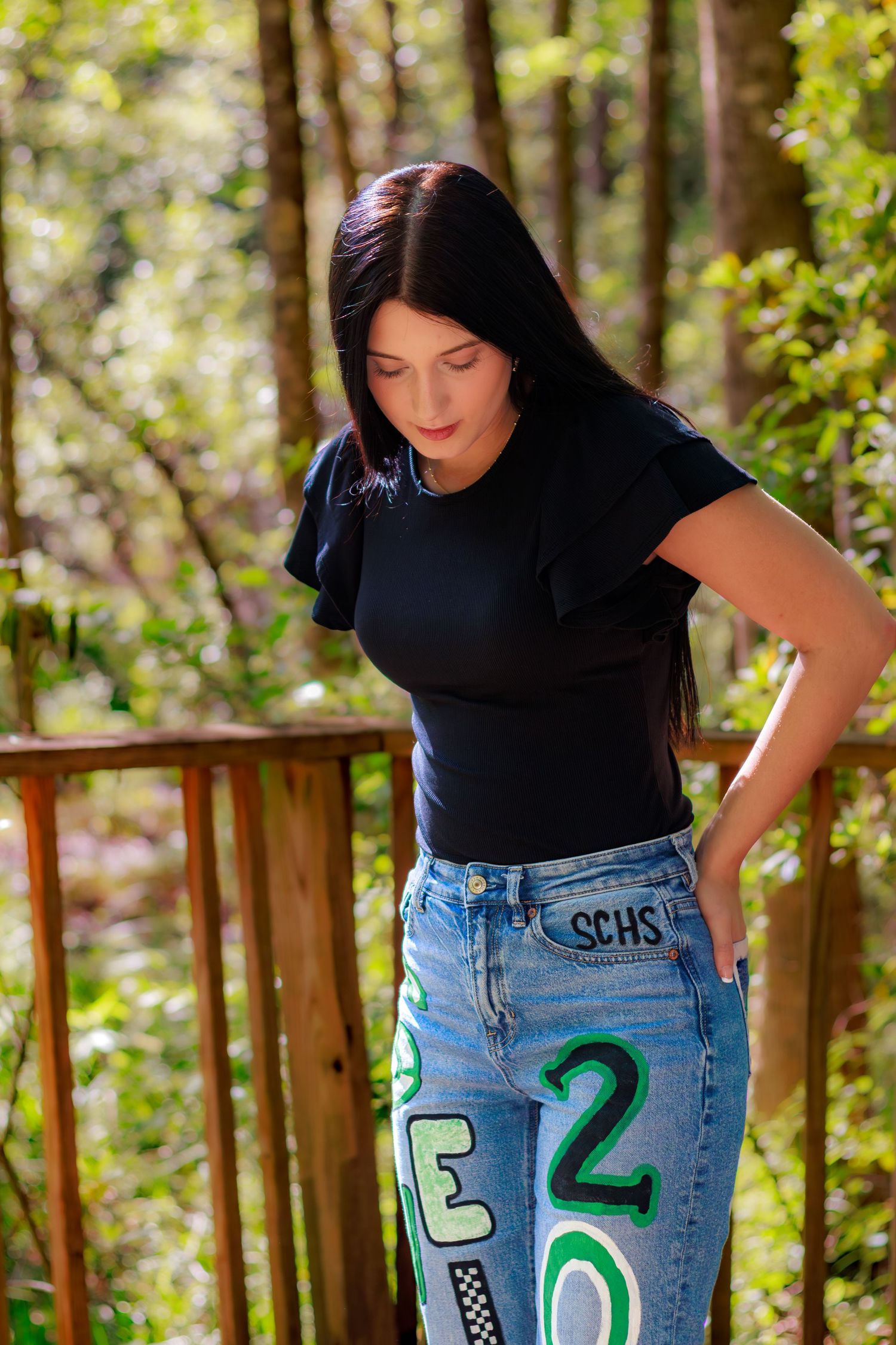 Young woman with long dark hair wearing black top and painted jeans with SCHS text outdoors.
