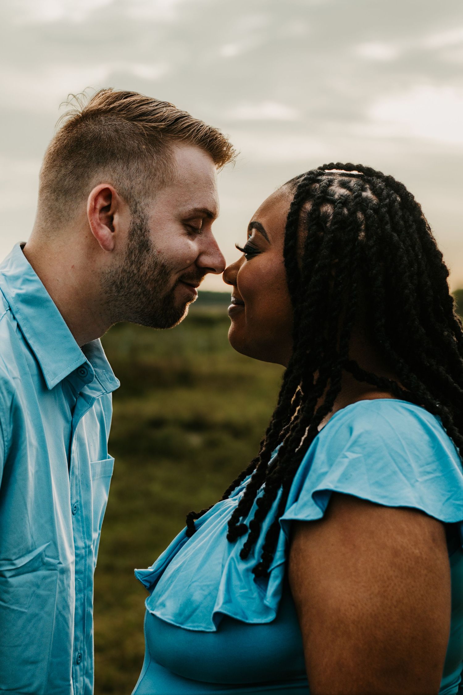 Interracial couple in blue outfits sharing romantic moment outdoors.