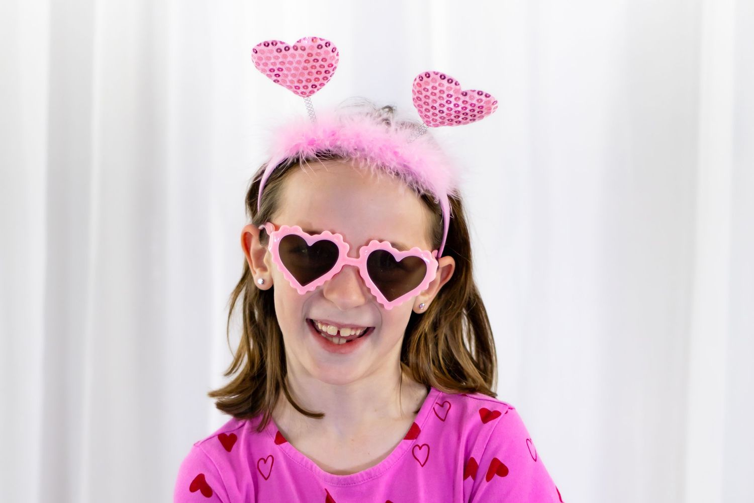 Laughing girl wearing pink heart sunglasses and sparkly heart headband in pink Valentine's Day outfit.