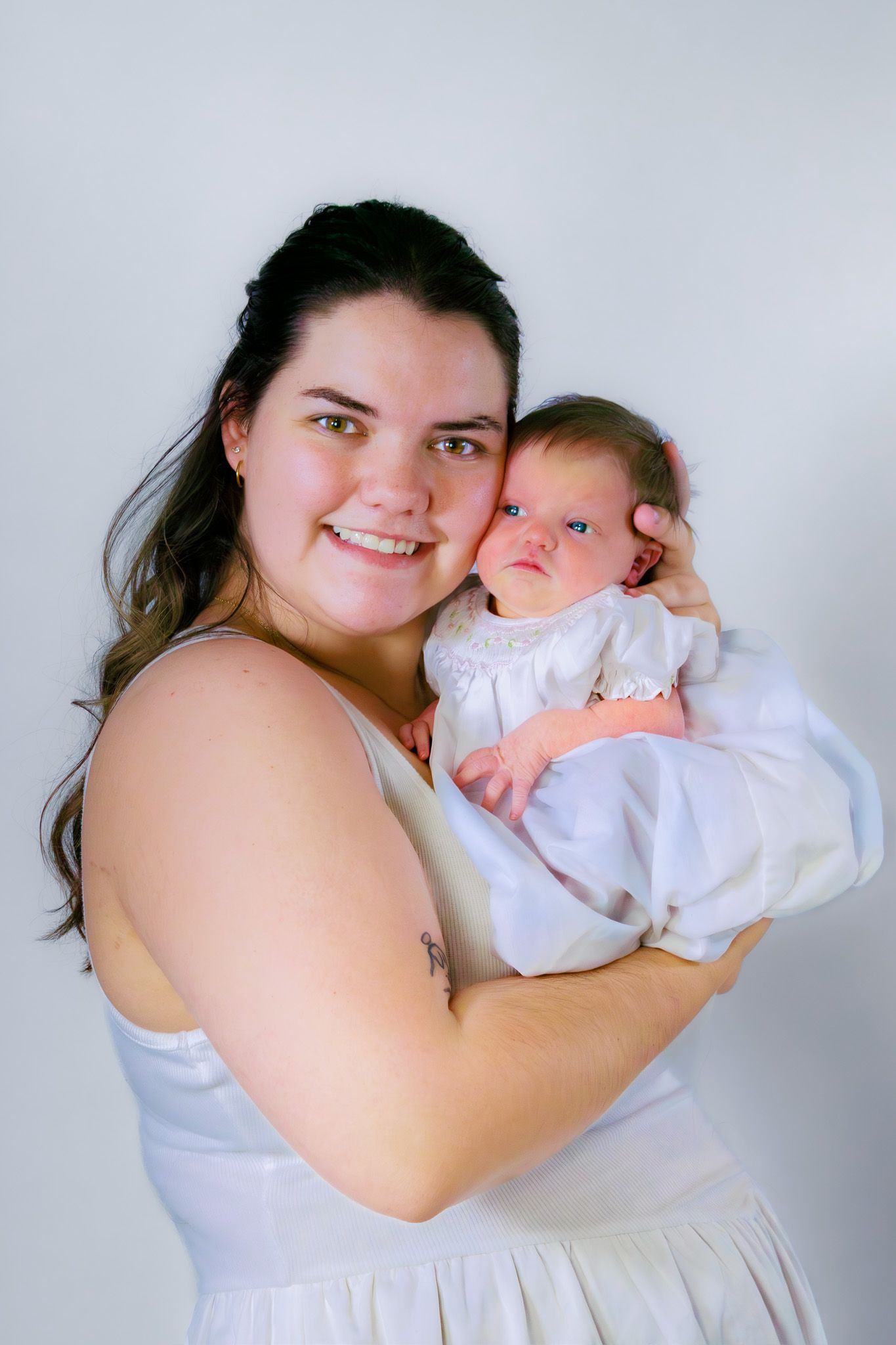 Smiling mother in white dress proudly holding her alert newborn baby close.