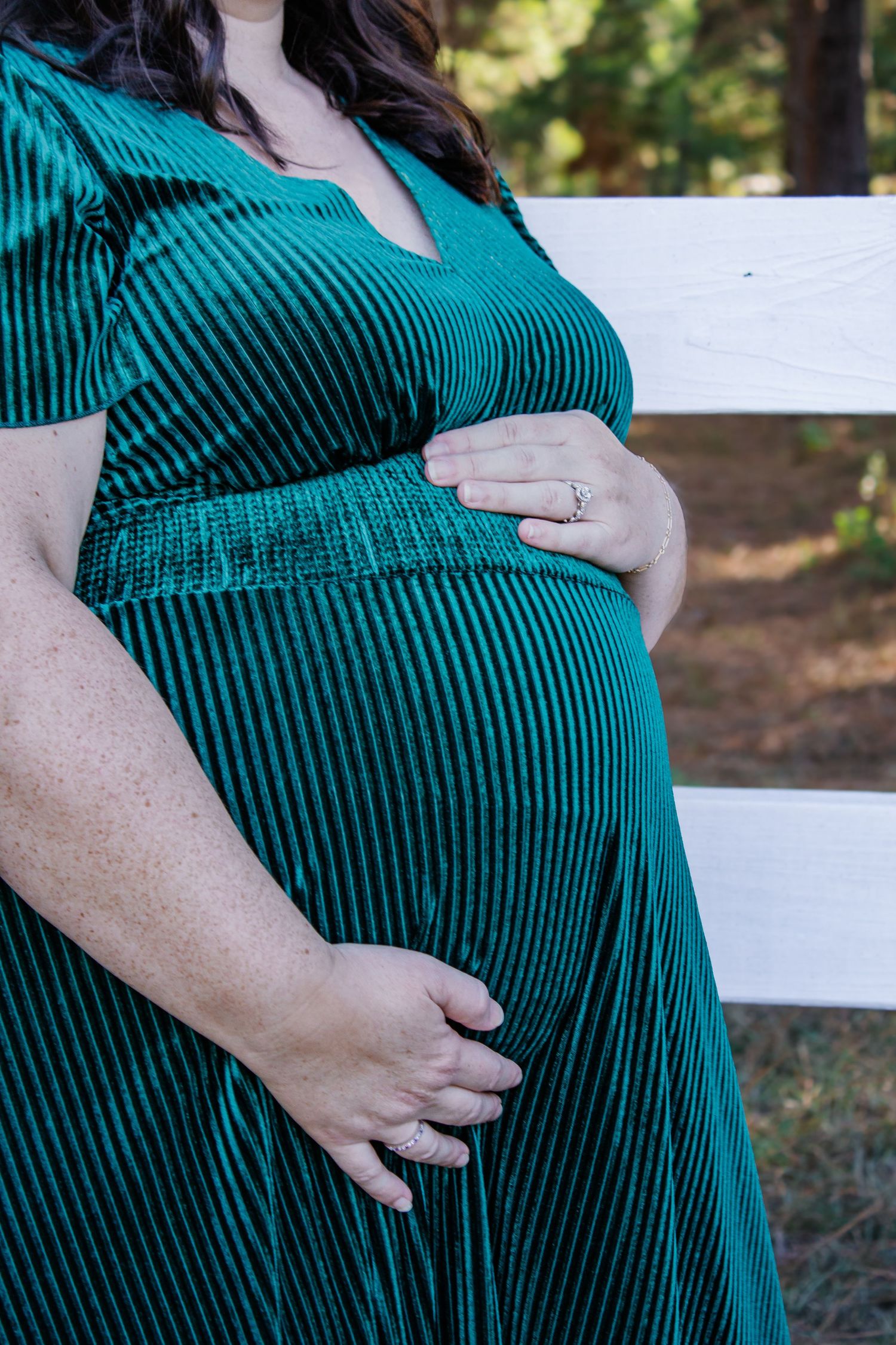 Close-up of pregnant belly in teal striped velvet dress with hands cradling bump.