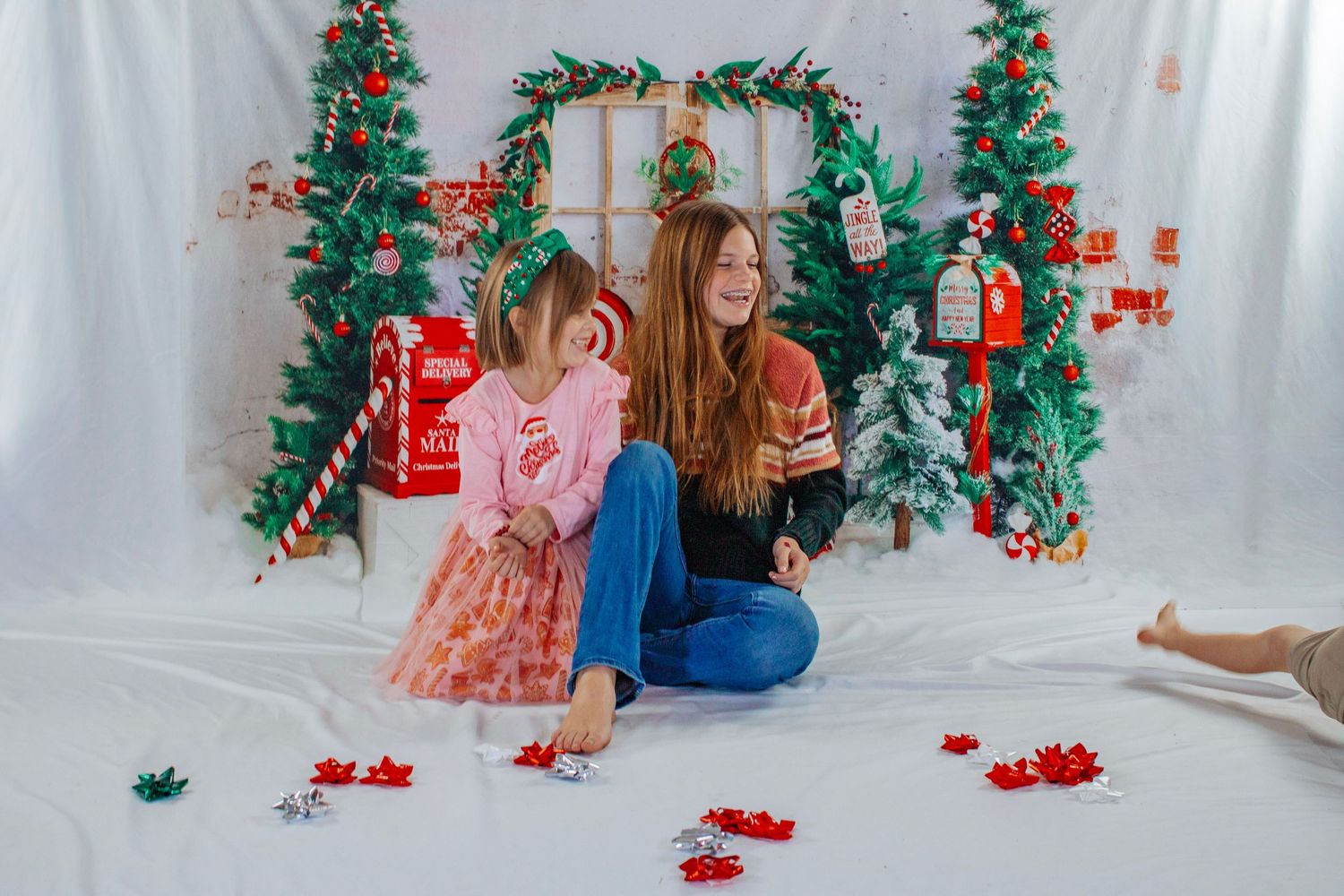 A mother and young daughter sit together laughing surrounded by Christmas decorations and scattered star confetti.