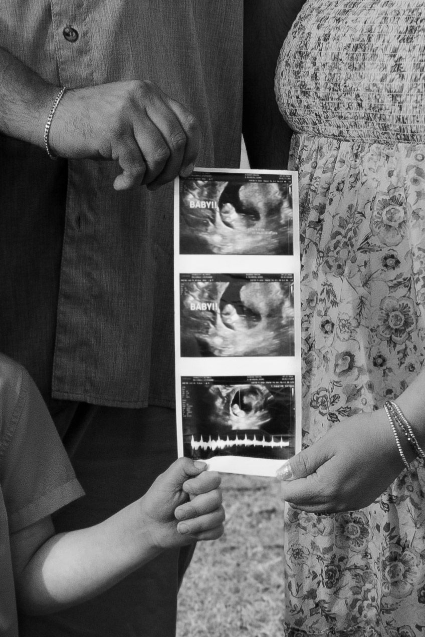 Black and white photo of family holding ultrasound strip for pregnancy reveal.