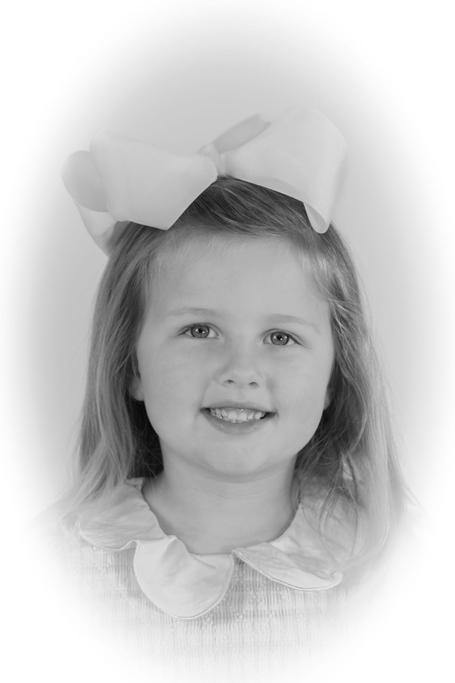 Black and white portrait of a young girl with long hair wearing a large white bow and collared dress, smiling sweetly.