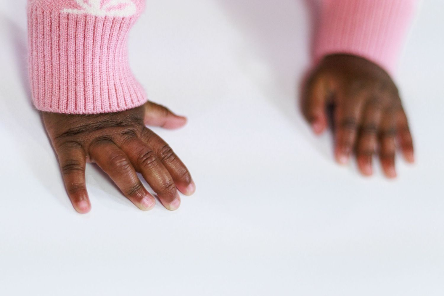 Close-up of a child's hands in pink sweater sleeves resting on a white surface.