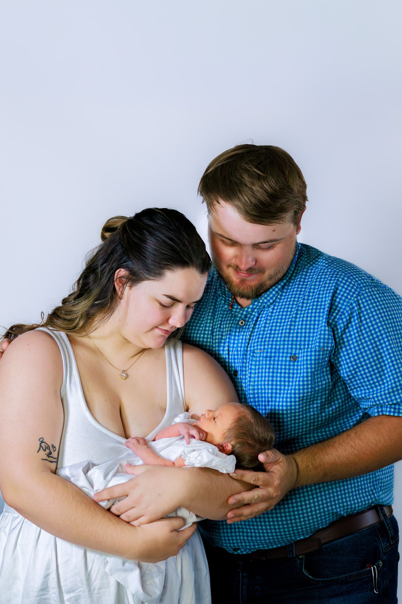 New parents lovingly gazing at their newborn baby, mother in white dress and father in blue shirt.