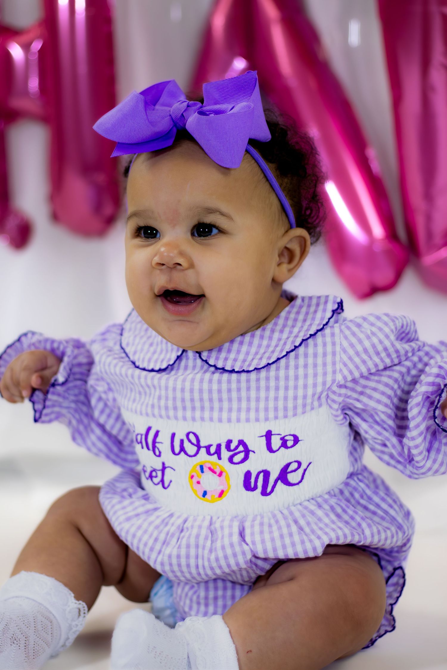 Close-up of baby girl in purple gingham romper reading Half Way to Sweet One at birthday shoot.