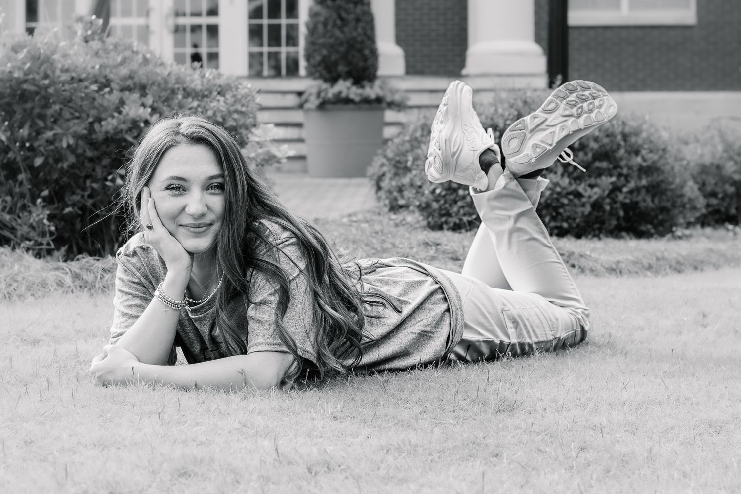 Young woman with long hair lies on grass smiling in black and white outdoor portrait.