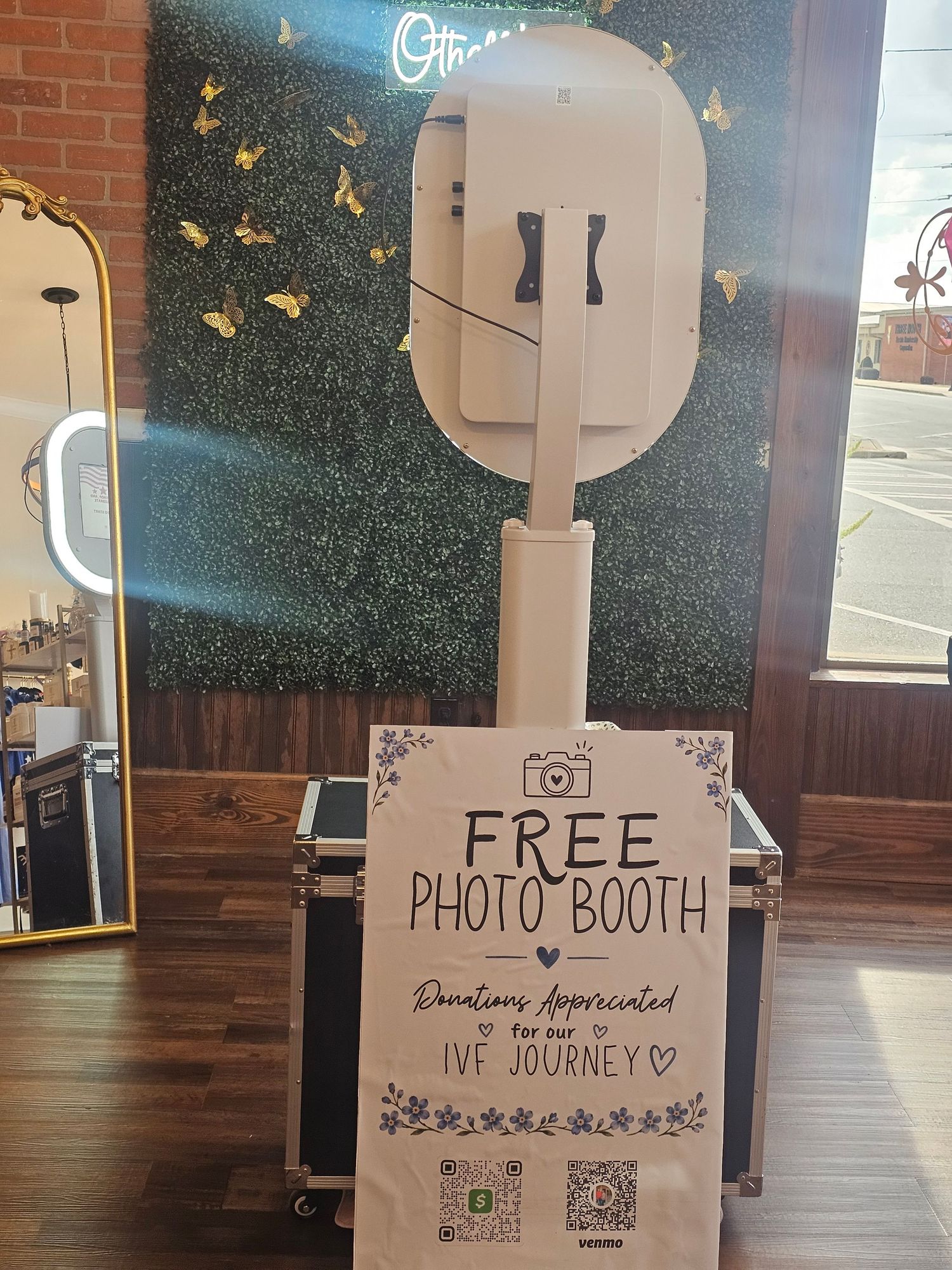 Free photo booth on a stand with a sign requesting donations for an IVF journey, set up inside a decorated venue.