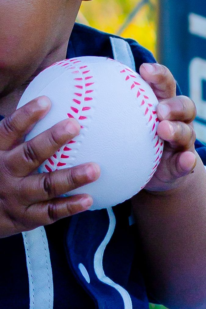 Close-up of hands gripping a white baseball with red stitching, held against a player's chest in a dugout.